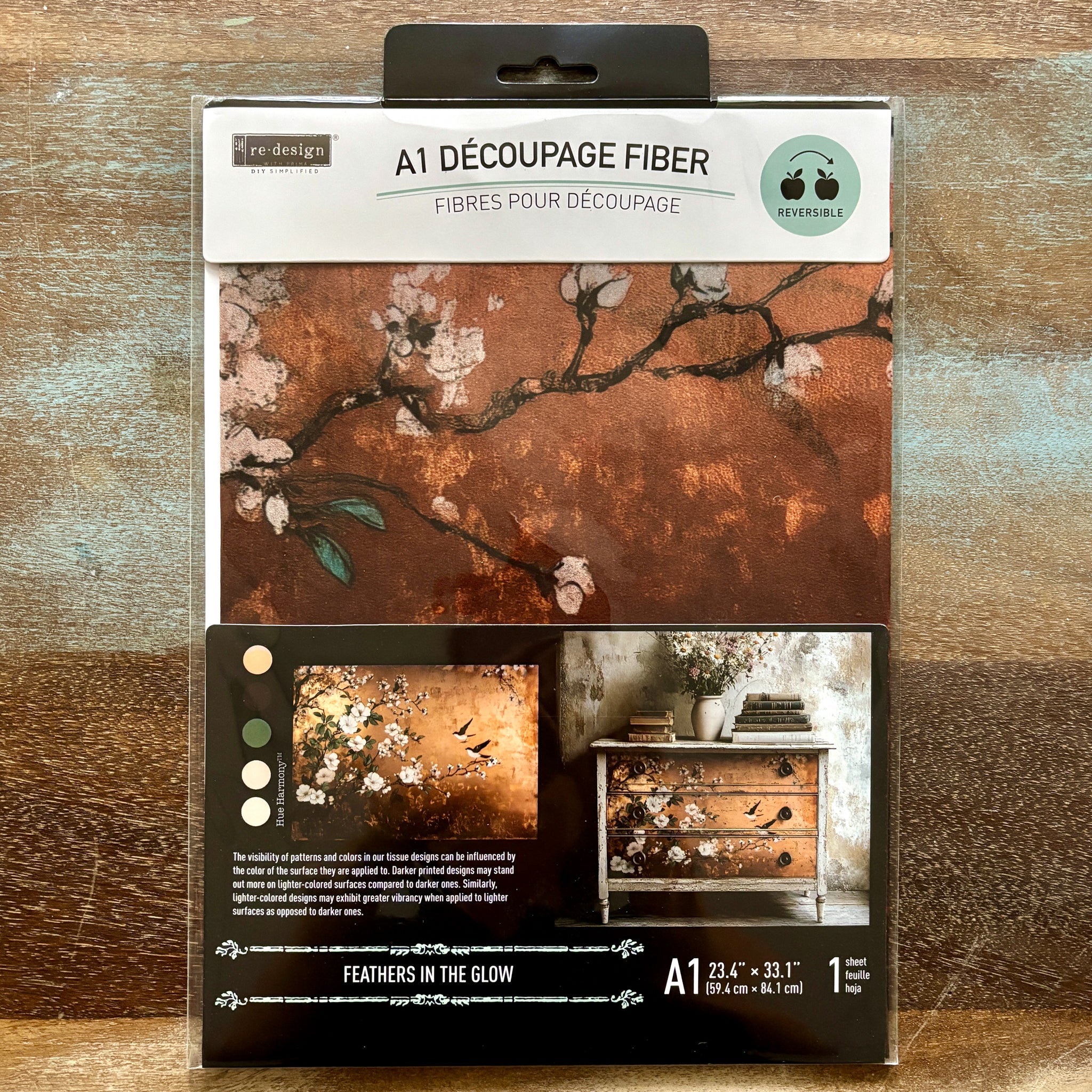 A package of ReDesign with Prima's Feathers in the Glow A1 fiber paper is against a wood background.