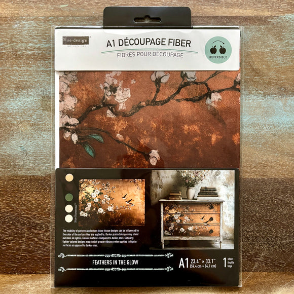 A package of ReDesign with Prima's Feathers in the Glow A1 fiber paper is against a wood background.