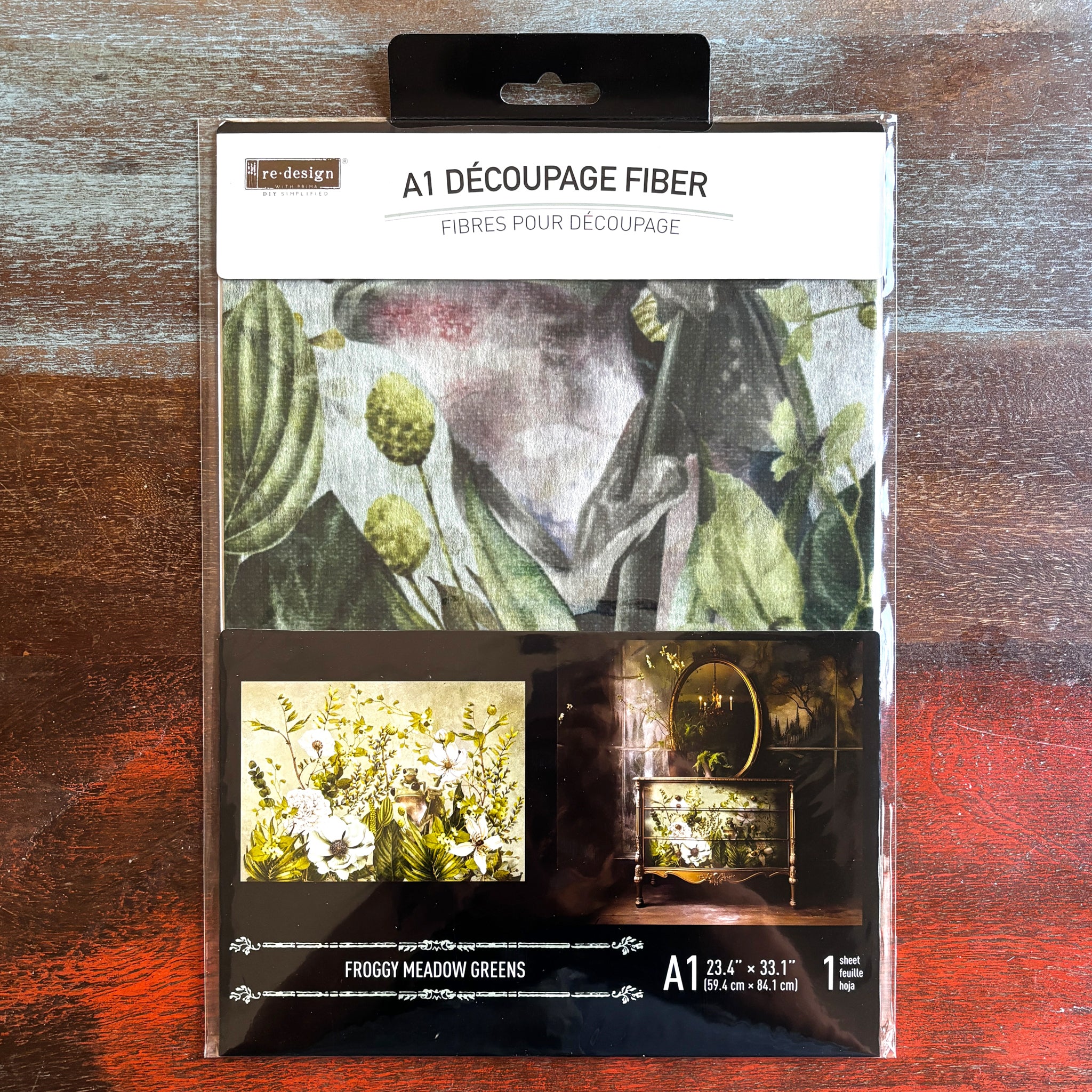 A package of ReDesign with Prima's Froggy Meadow Greens fiber paper is against a dark wood background.