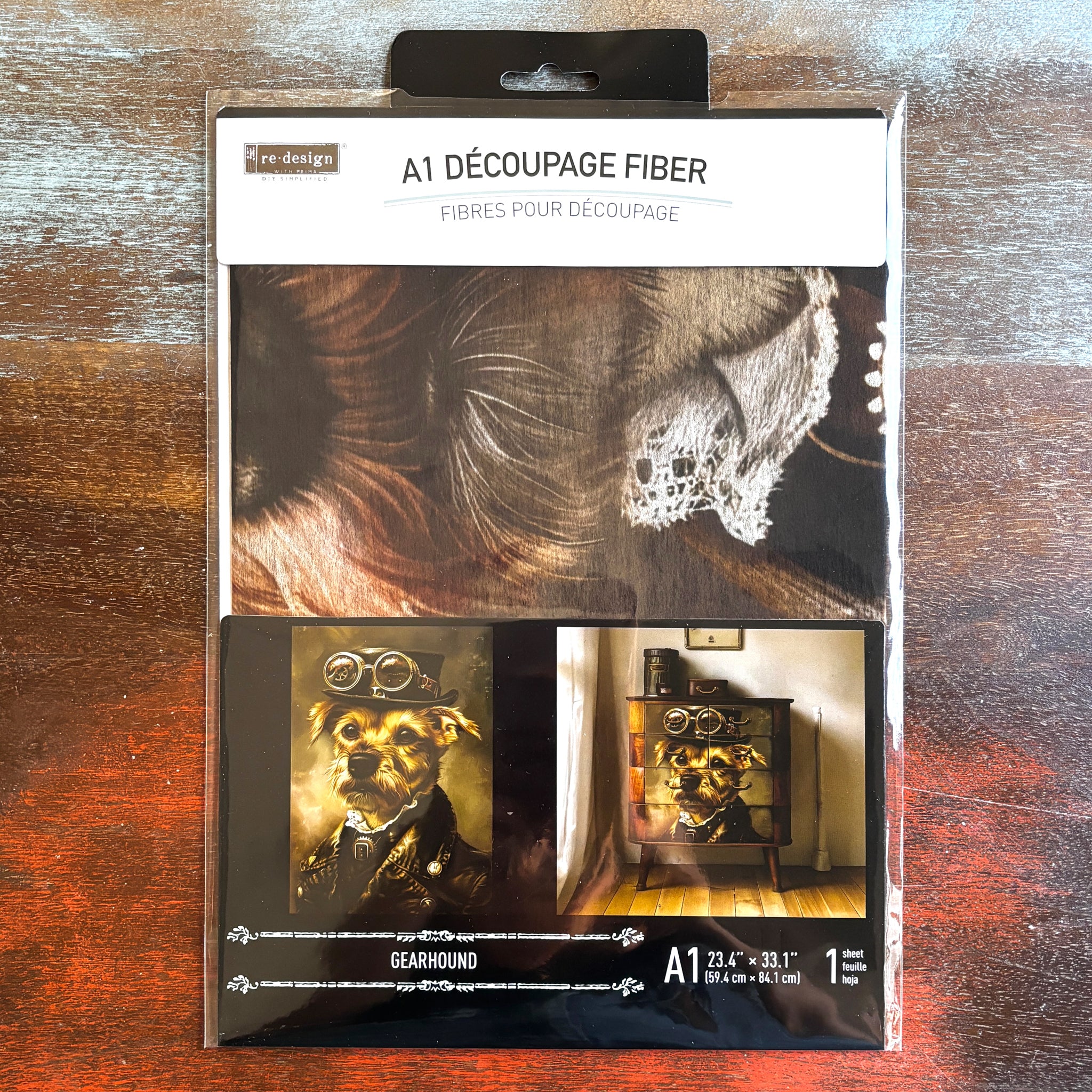 A package of ReDesign with Prima's Gear Hound A1 fiber paper is against a dark wood background.