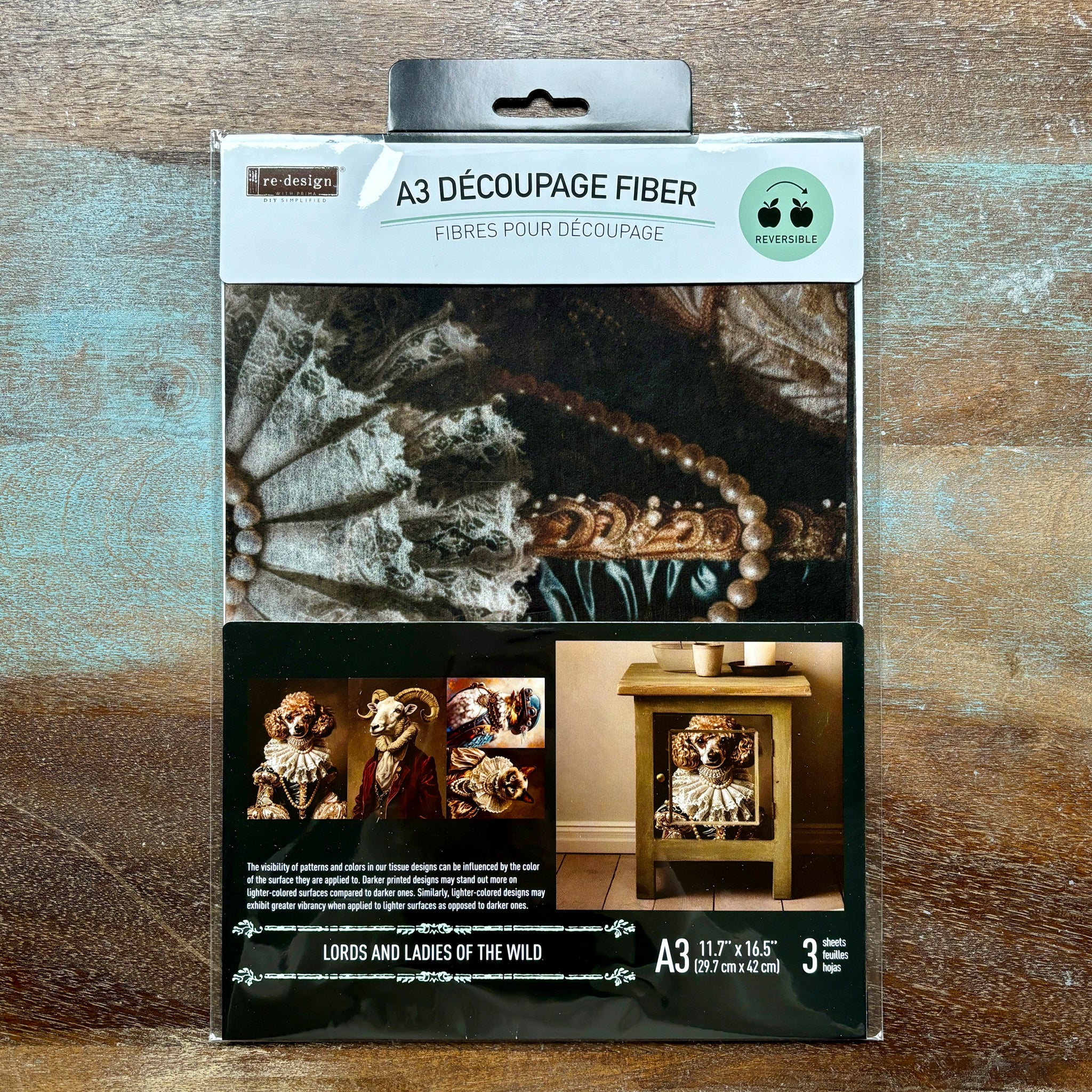 A package of ReDesign with Prima's Lords and Ladies of the Wild A3 fiber paper 3 pack is against a wood background.