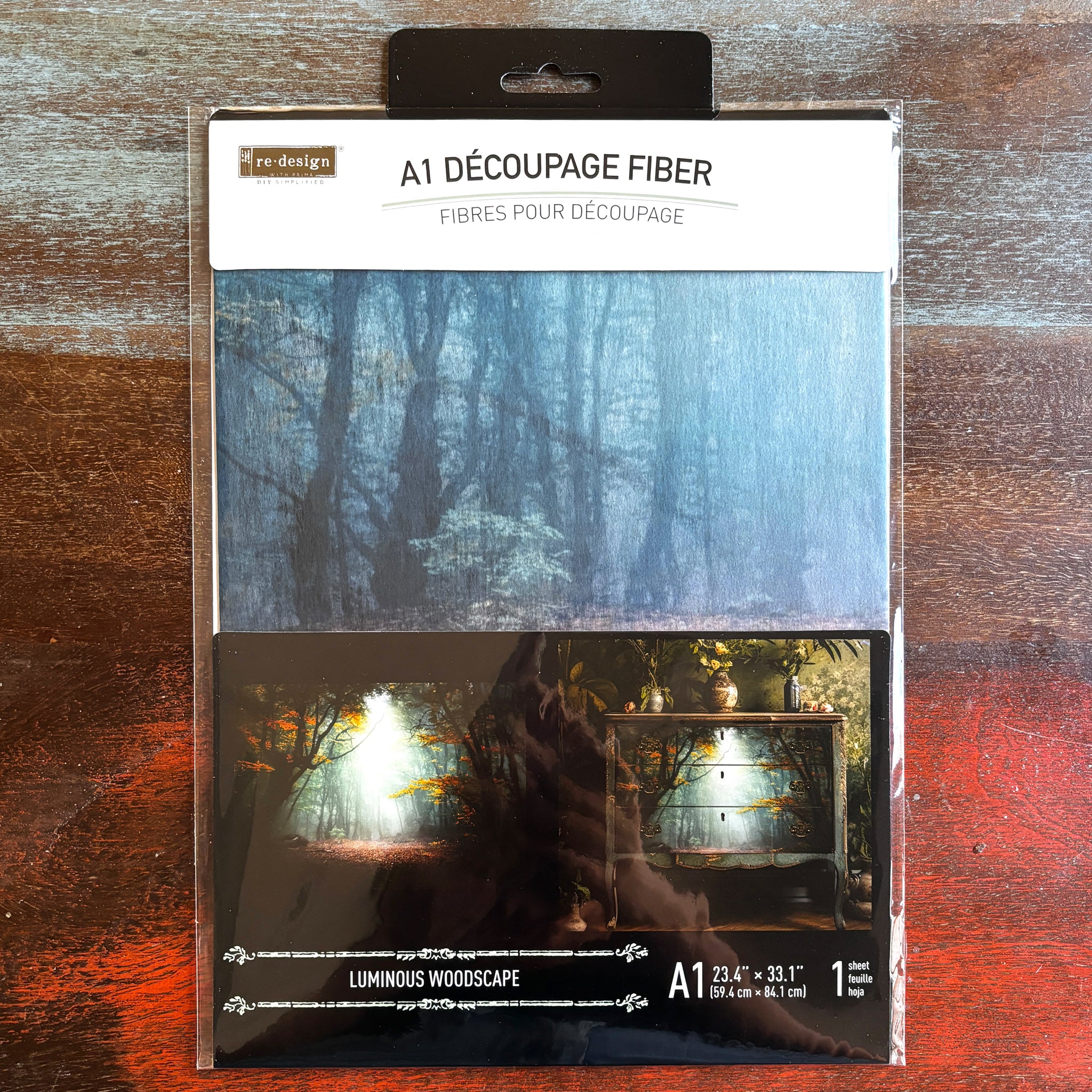 A package of ReDesign with Prima's Luminous Woodscape A1 fiber paper is against a dark wood background.