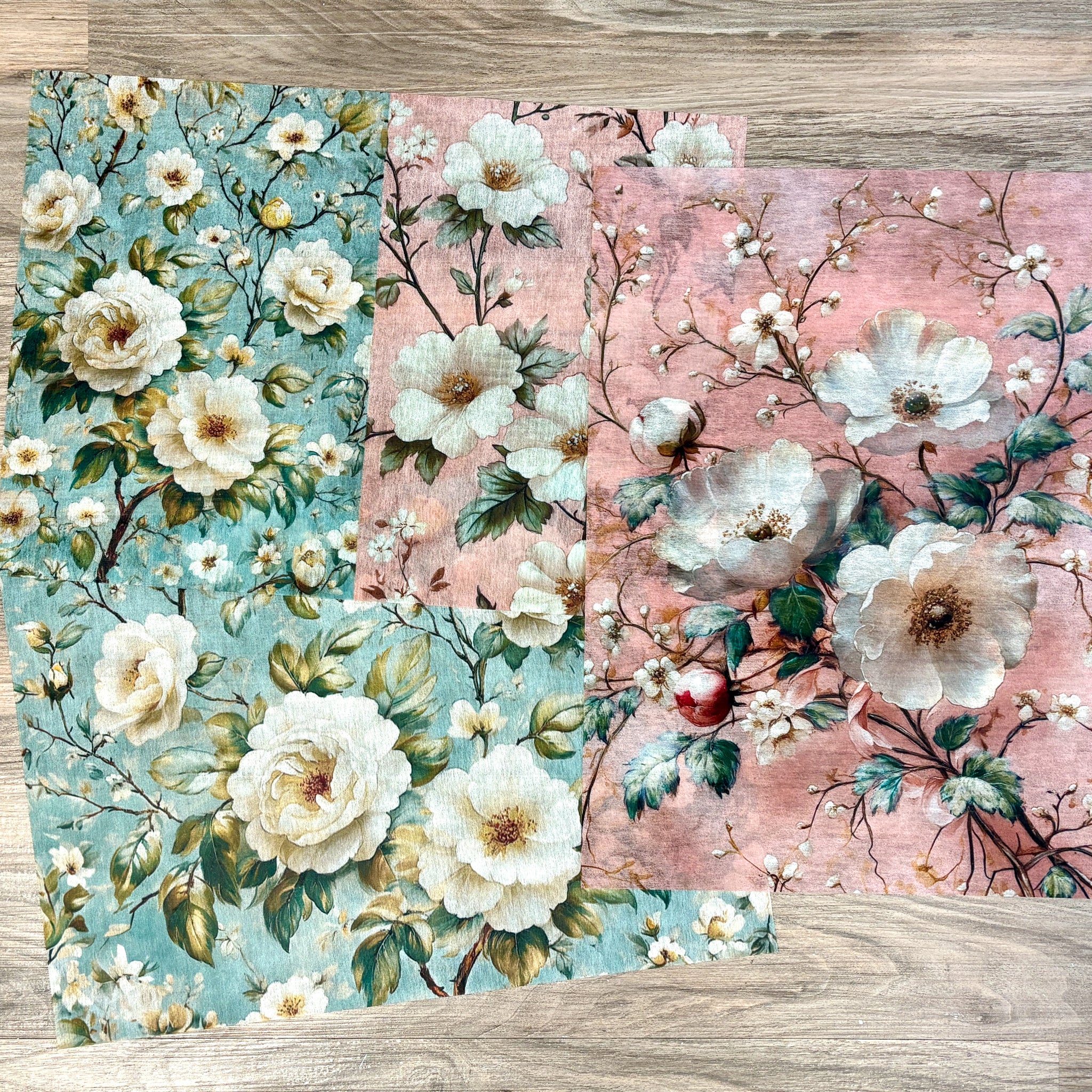 Three sheets of A3 fiber papers featuring beautiful white flowers against light pink and light teal blue backdrops are against a light wood background.