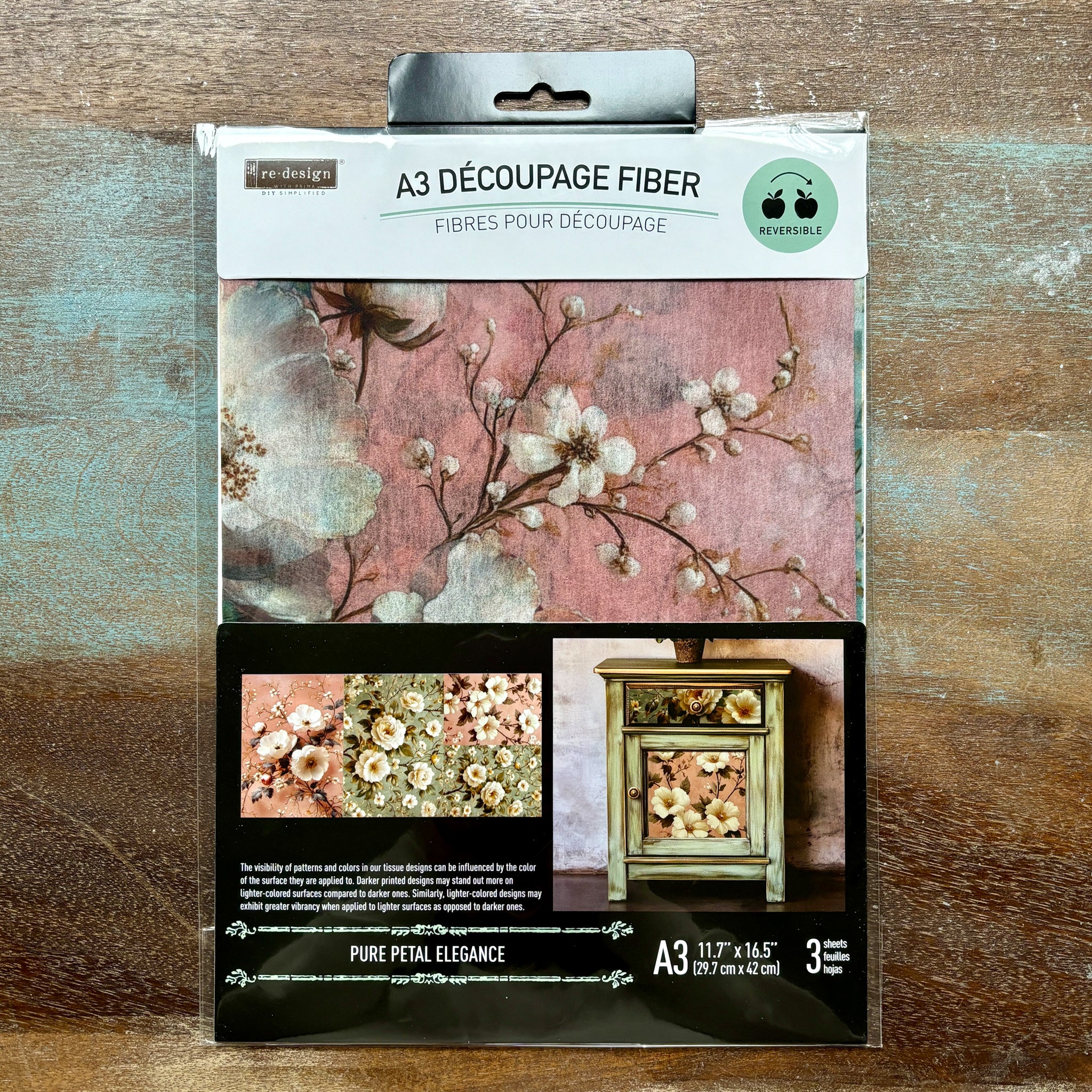 A package of ReDesign with Prima's Pure Petal Elegance A3 fiber paper 3 pack is against a wood background.