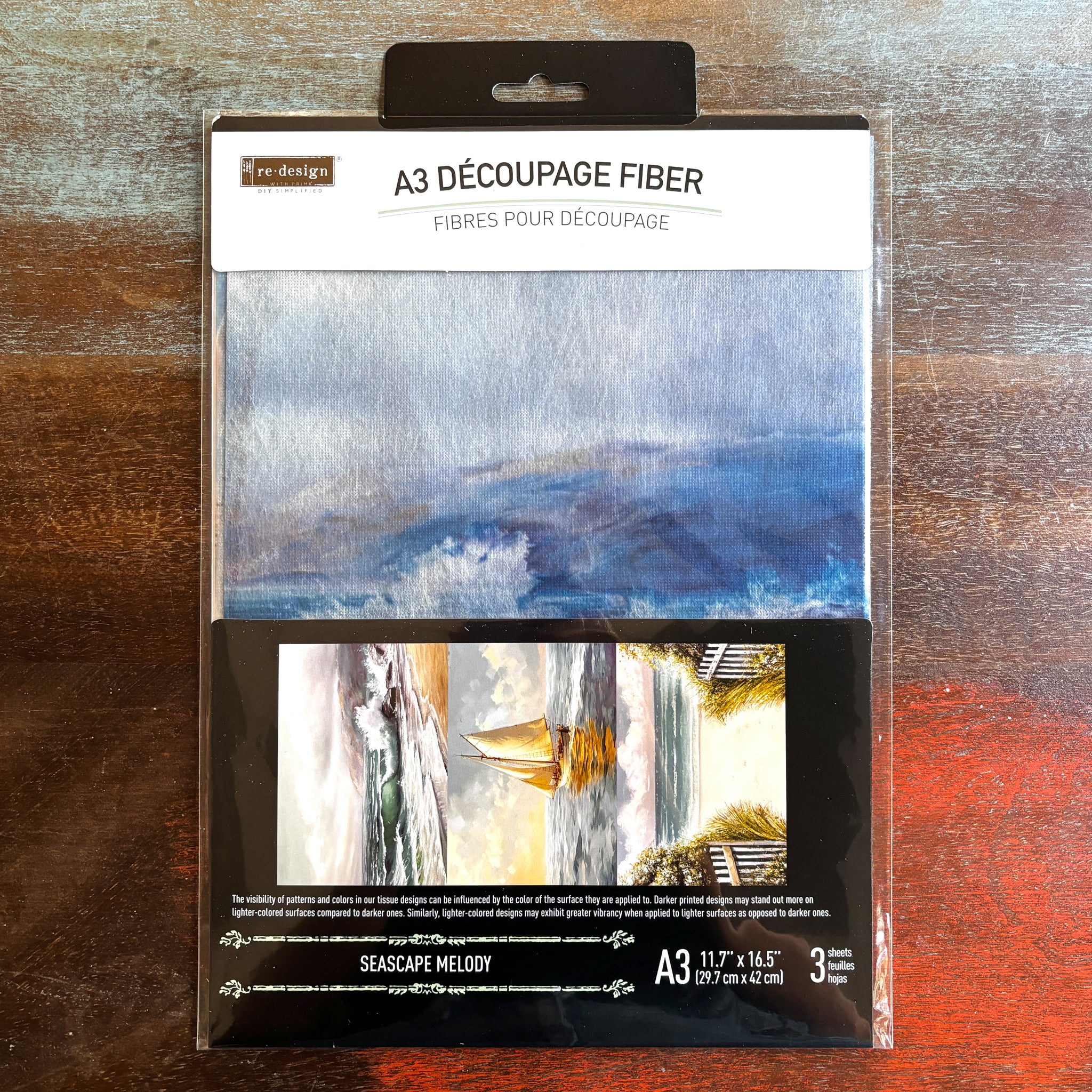 A package of ReDesign with Prima's Seascape Melody fiber paper is against a dark wood background.