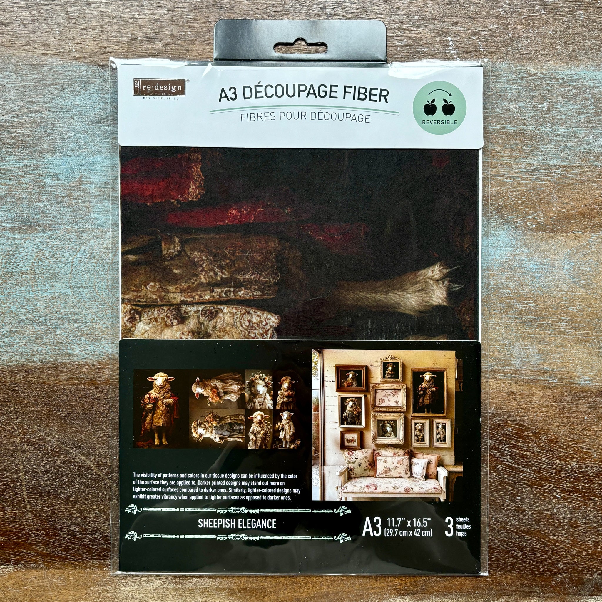 A package of ReDesign with Prima's Sheepish Elegance A3 fiber paper 3 pack is against a wood background.