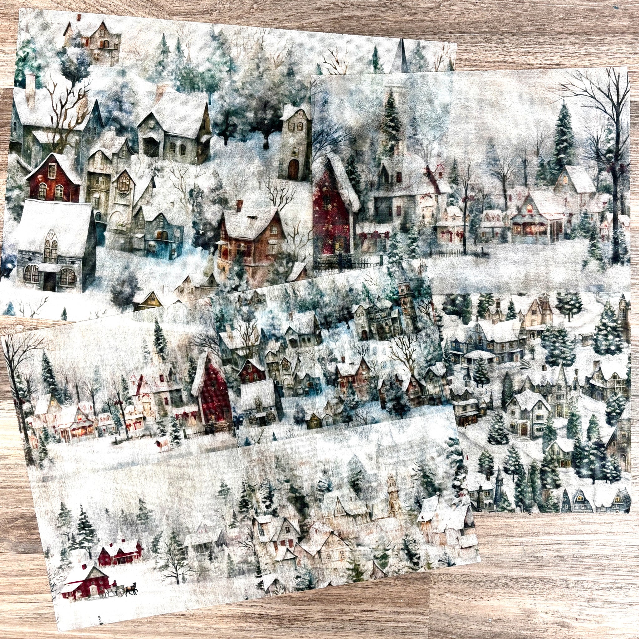 Three sheets of A3 fiber papers featuring quiet snowy villages are against a light wood background.