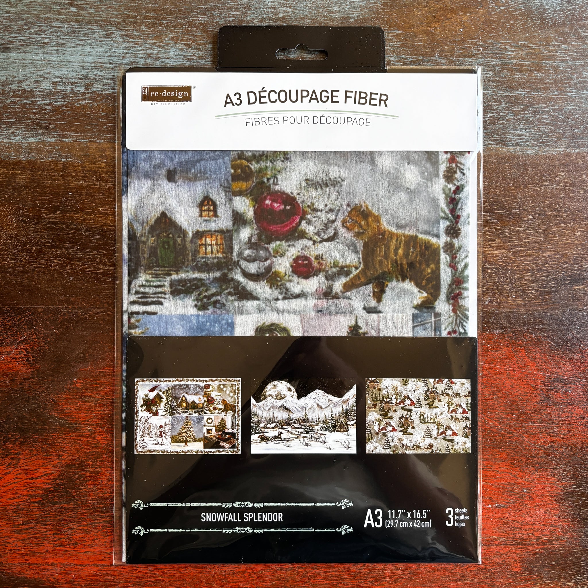 A package of ReDesign with Prima's Snowfall Splendor A3 fiber paper 3 pack is against a dark wood background.