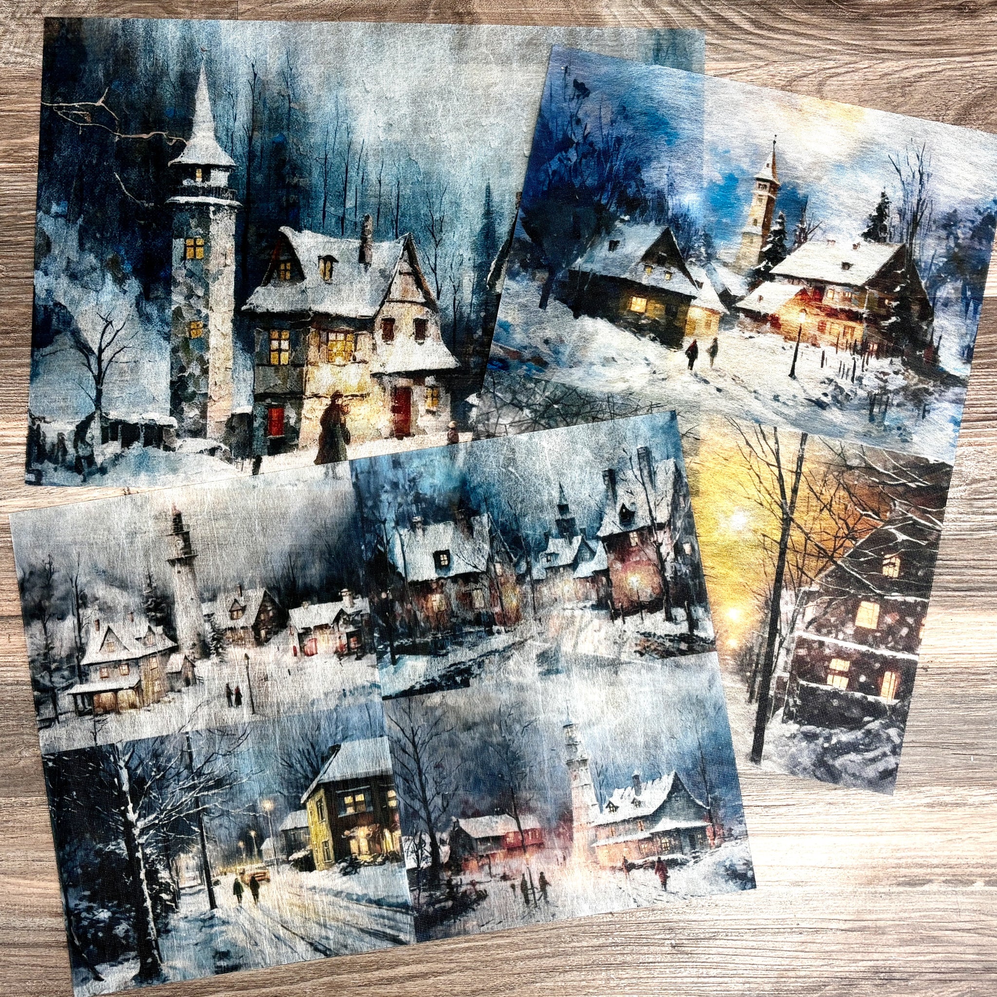 Three sheets of A3 fiber papers featuring evening scenes of snow covered villages are against a light wood background.