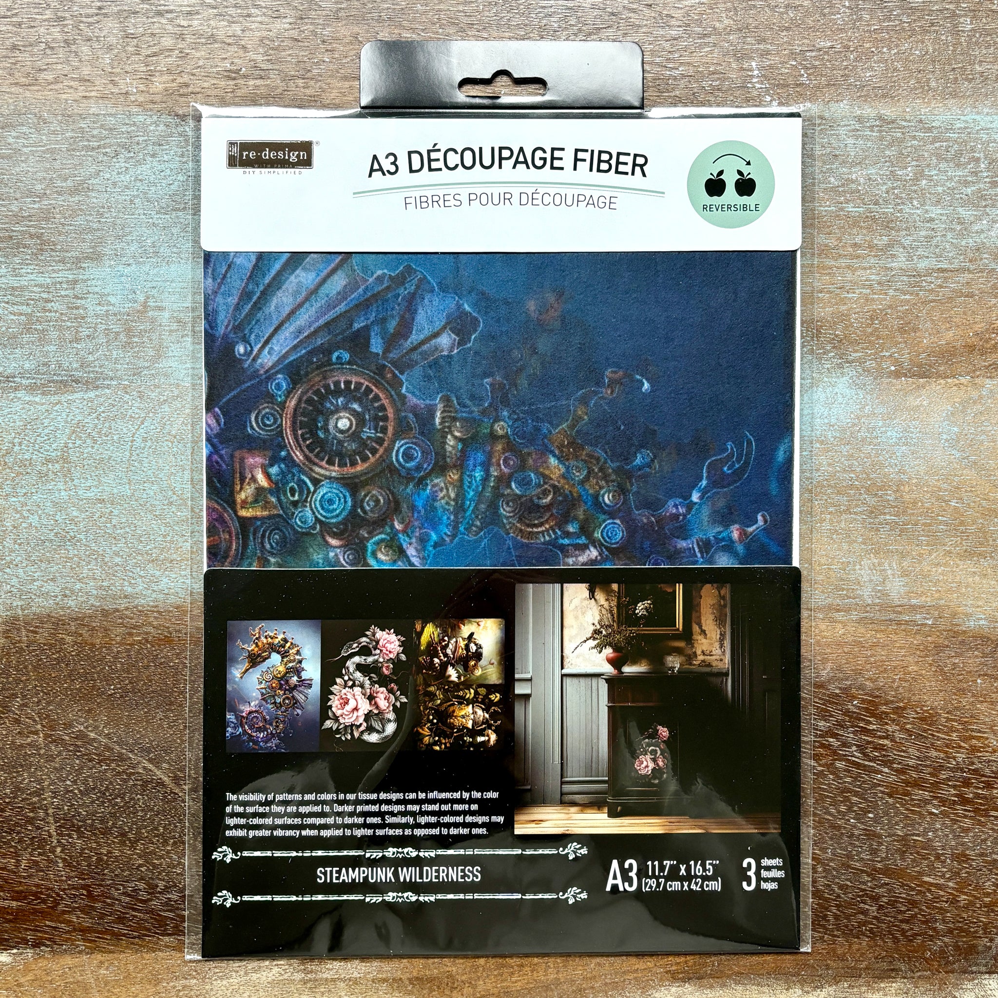 A package of ReDesign with Prima's Steampunk Wilderness A3 fiber paper 3 pack is against a wood background.