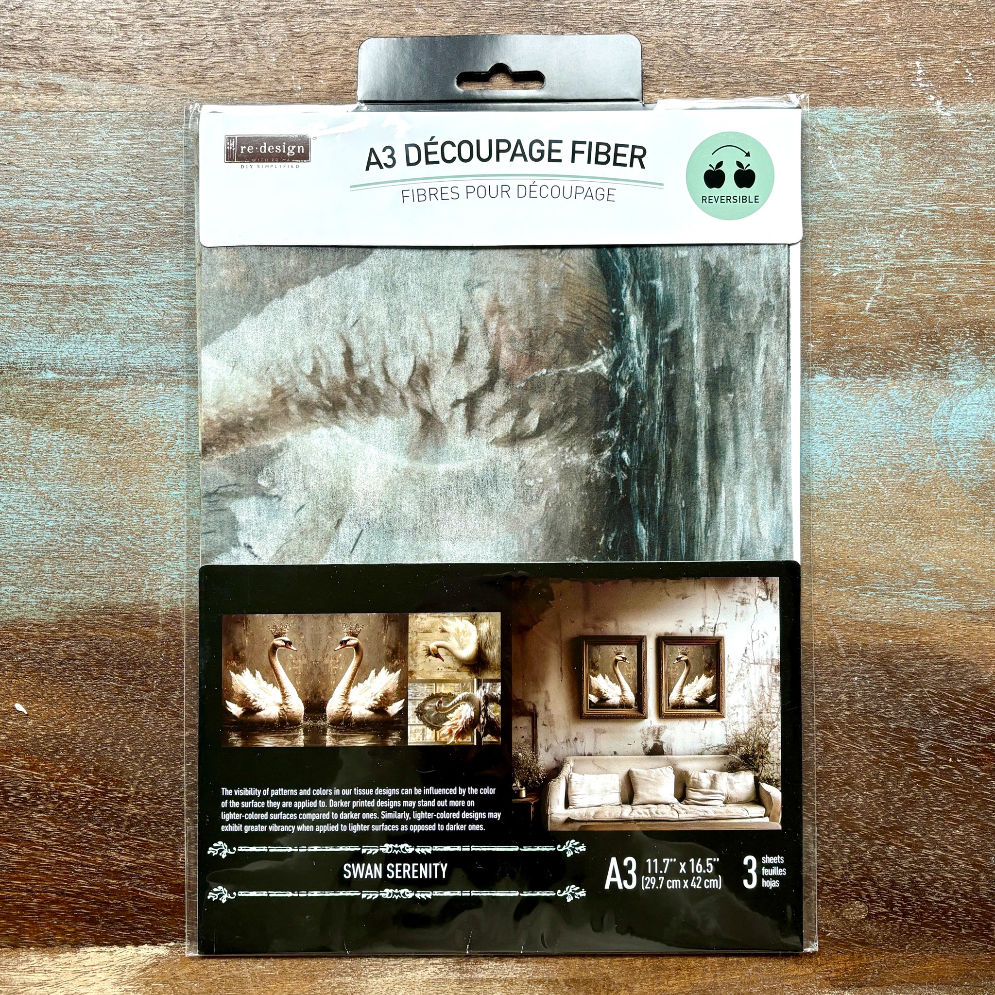 A package of ReDesign with Prima's Swan Serenity A3 fiber paper 3 pack is against a wood background.