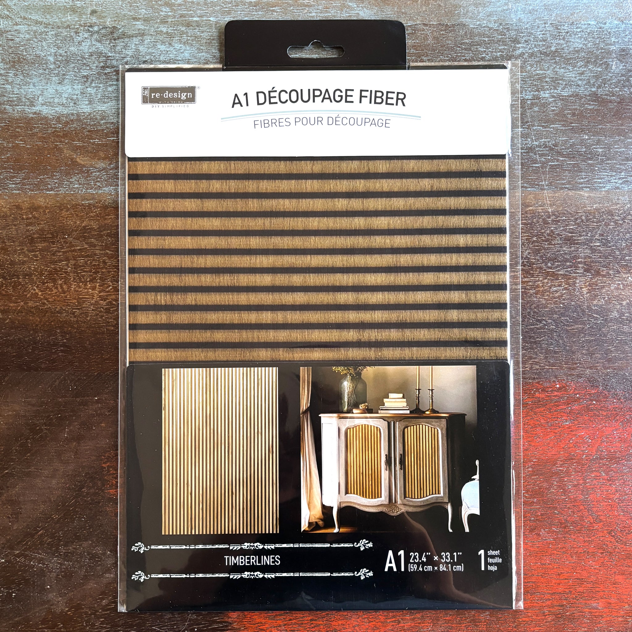 A package of ReDesign with Prima's Timberlines fiber paper is against a dark wood background.