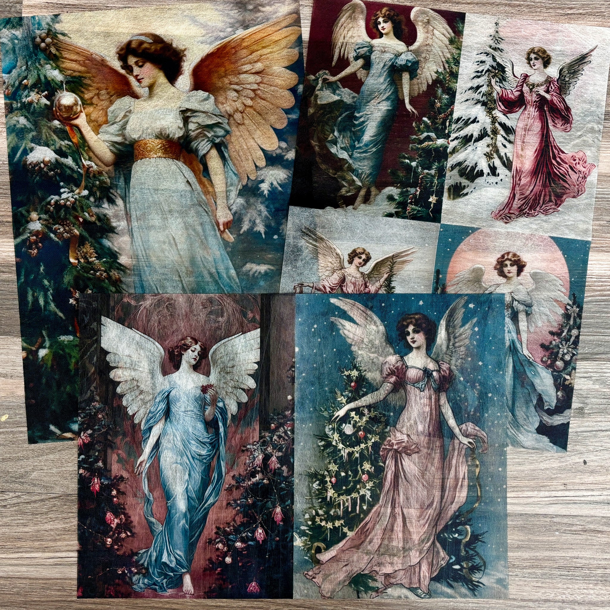 Three sheets of A3 fiber papers featuring vintage Victorian angels are against a light wood background.