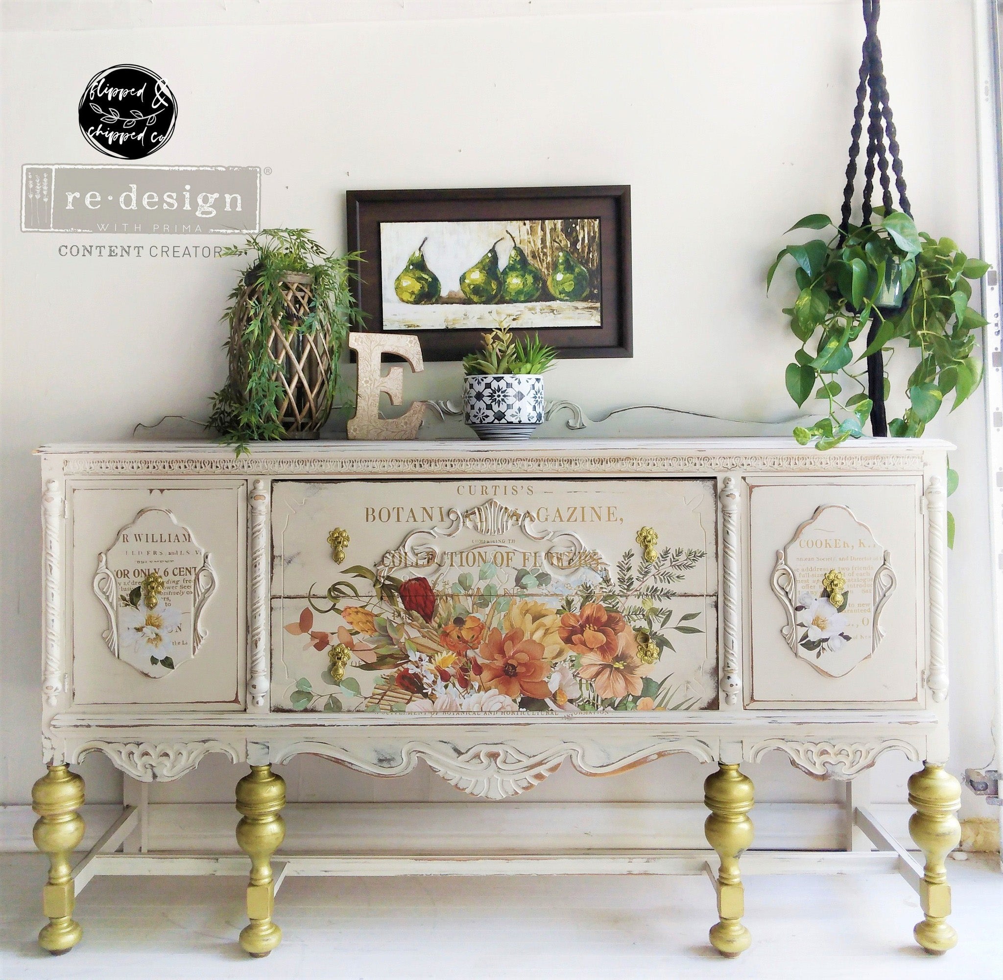 A vintage console table refurbished by Flipped & Chipped is painted soft white with gold legs and features ReDesign with Prima's Kacha Elegant Neutrals rub-on transfer on its 2 center drawers.