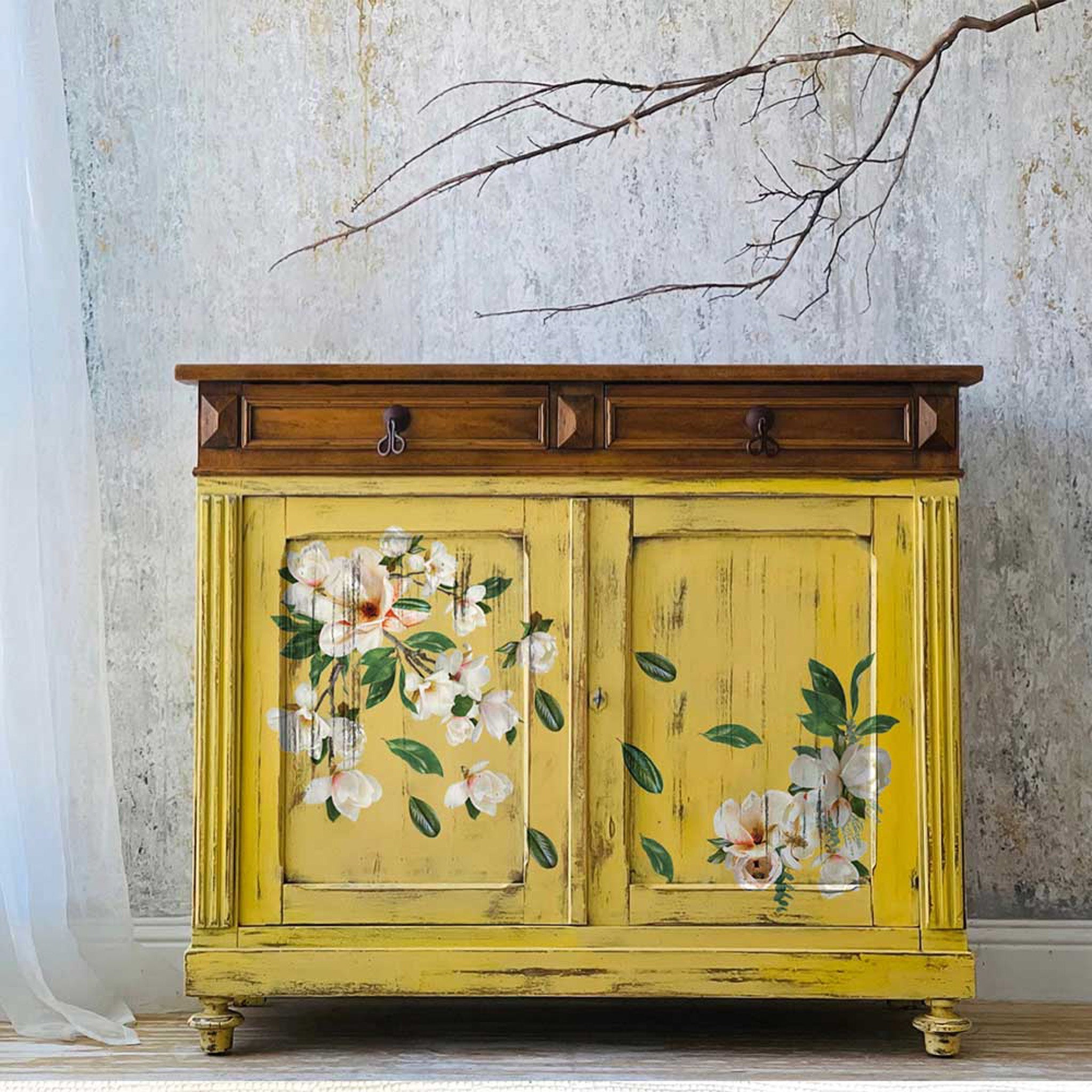 A small wood console table is painted yellow with natural wood stain and features ReDesign with Prima's La Gran Magnolia small transfer on its doors.