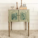 A vintage console table with 2 doors is painted light green and features ReDesign with Prima's Magic Jungle small transfer on its doors.