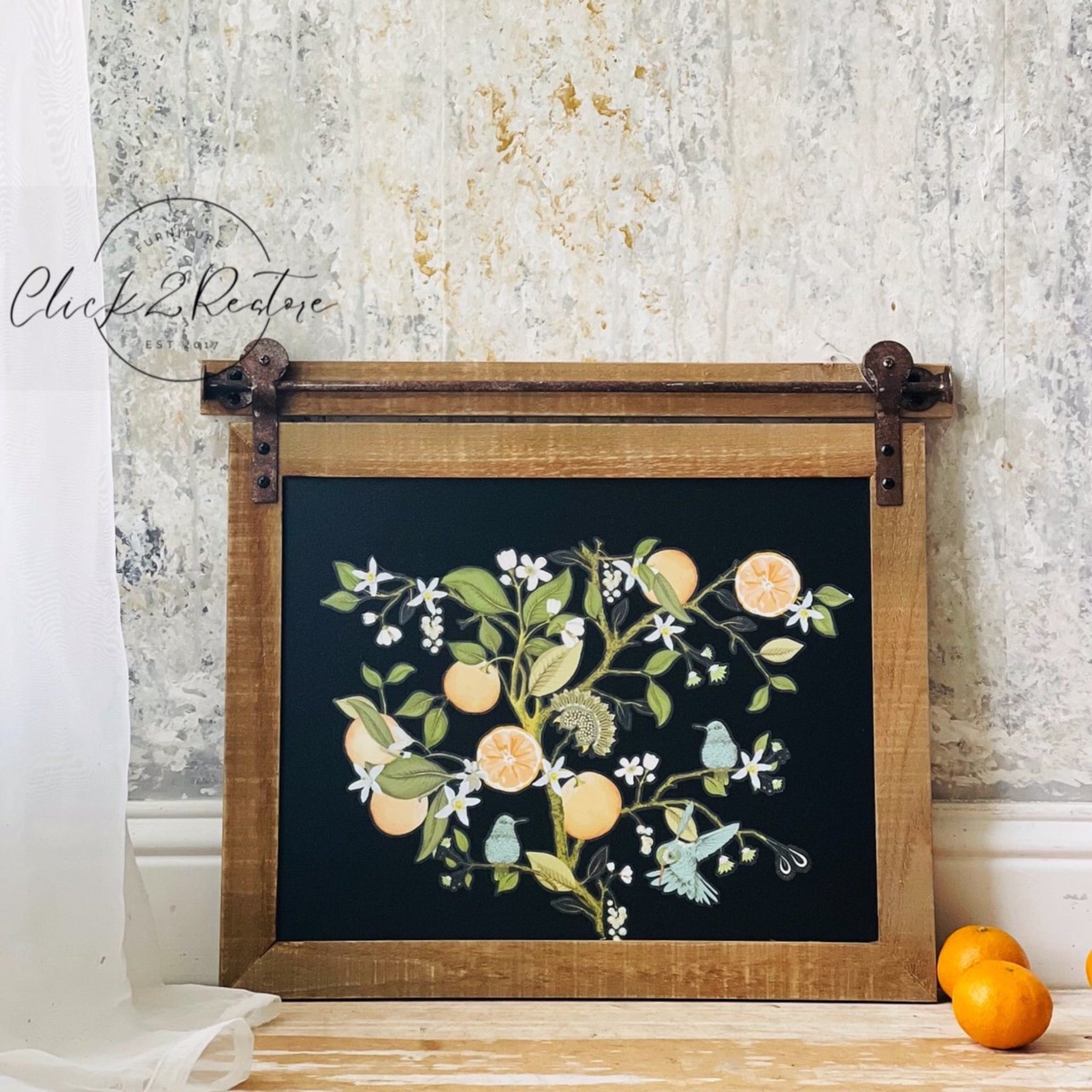 A vintage natural wood sliding cabinet door refurbished by Click 2 Restore features ReDesign with Prima's Orange Grove transfer on a black painted inlay.