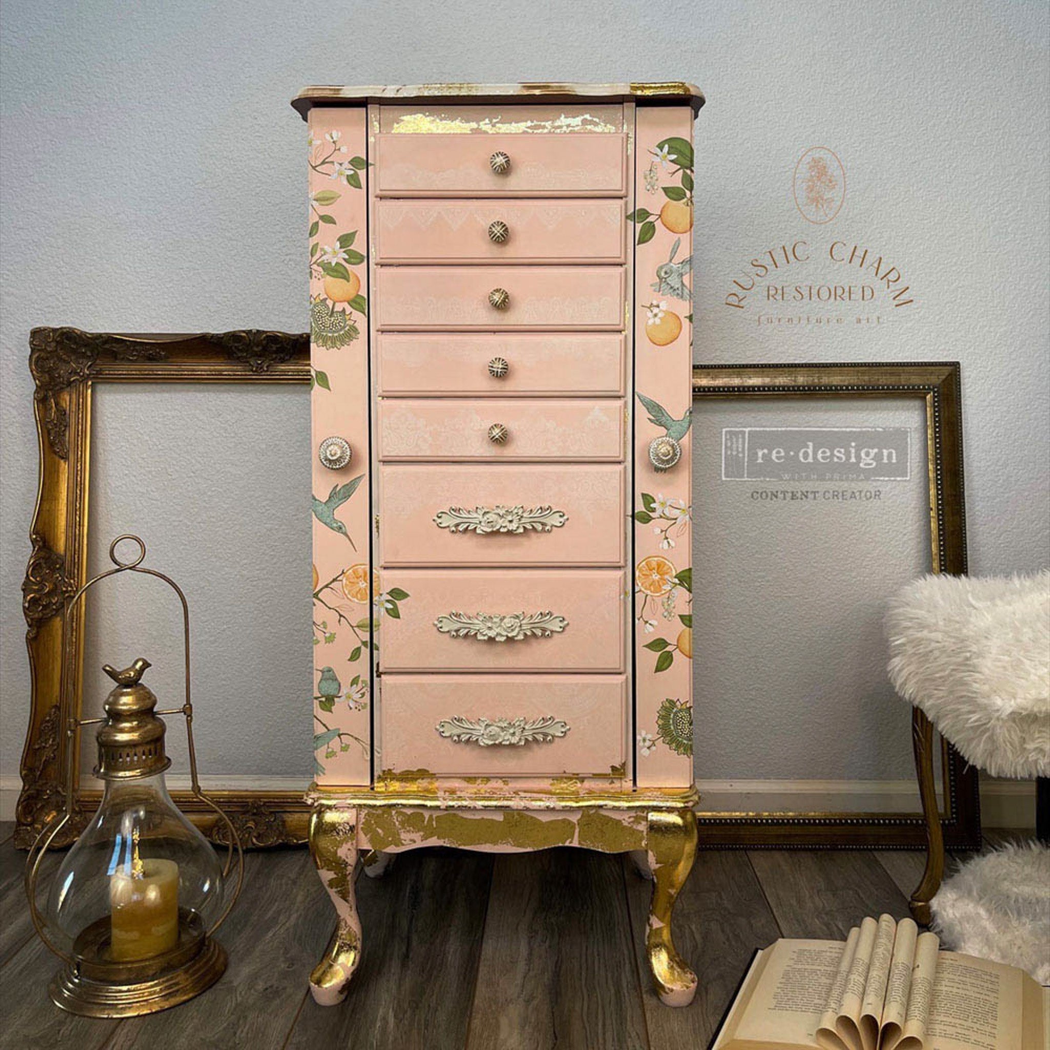 A tall vintage jewelry armoire refurbished by Rustic Charm Restored is painted peach with gold foil and features ReDesign with Prima's Orange Grove transfer on its 2 side doors.