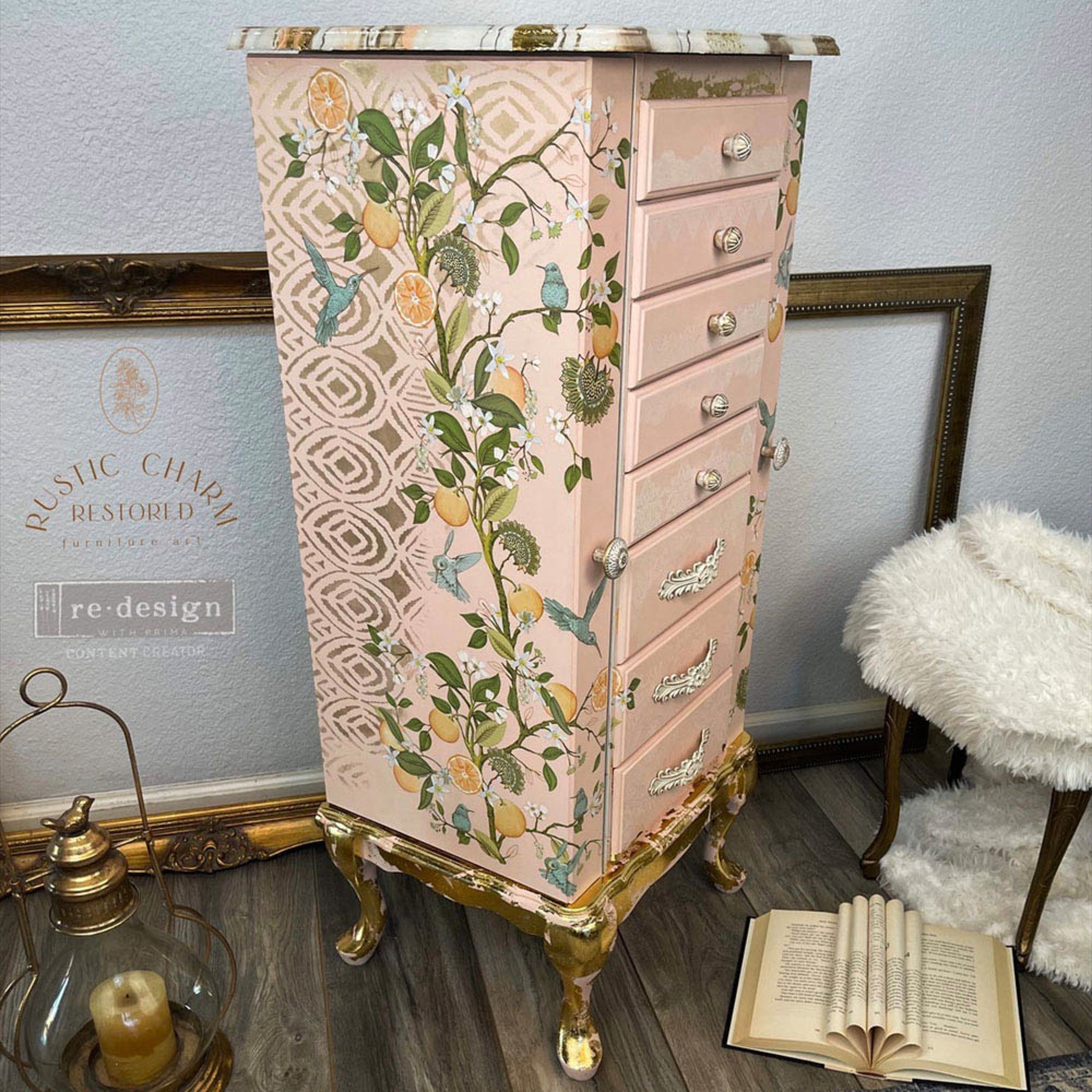 A corner view of a tall vintage jewelry armoire refurbished by Rustic Charm Restored is painted peach with gold foil and features ReDesign with Prima's Orange Grove transfer on its 2 side doors.