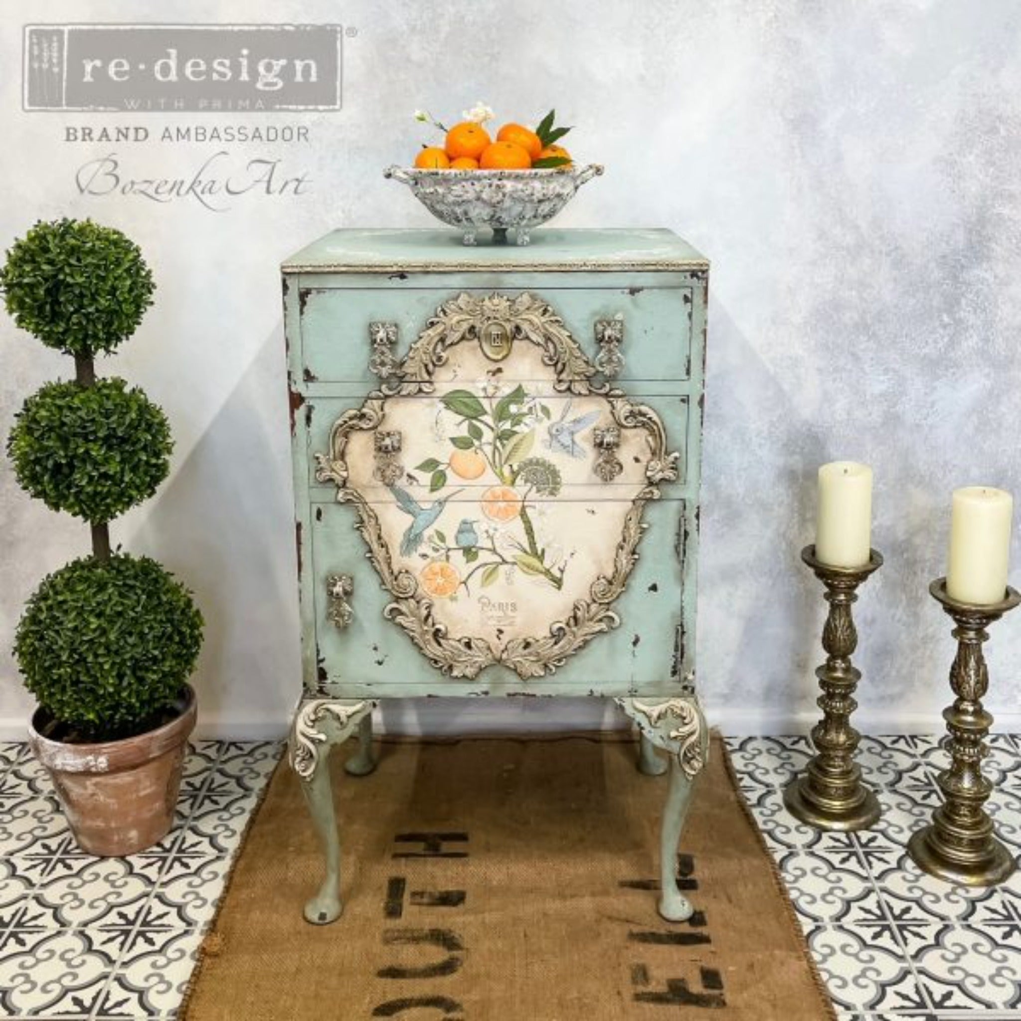 A vintage 3-drawer nightstand refurbished by Bozenka Art is painted soft teal blue and features ReDesign with Prima's Orange Grove transfer in the center of the drawers.