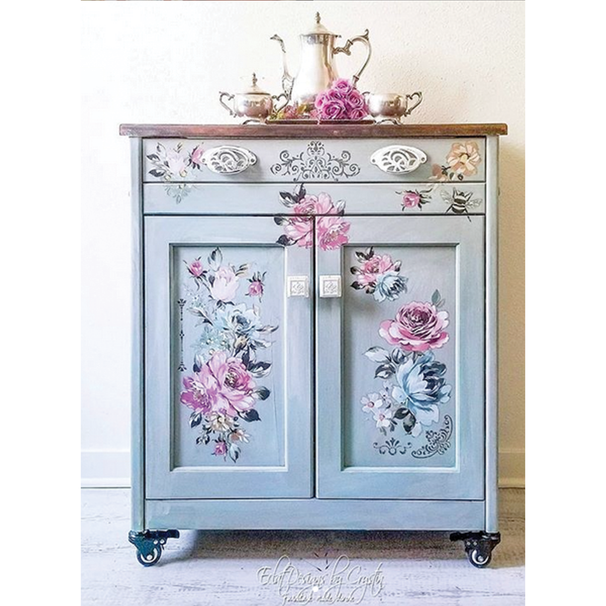 A small buffet cabinet is painted light blue-grey and features ReDesign with Prima's Fuchsia Sunset rub on transfer on it.