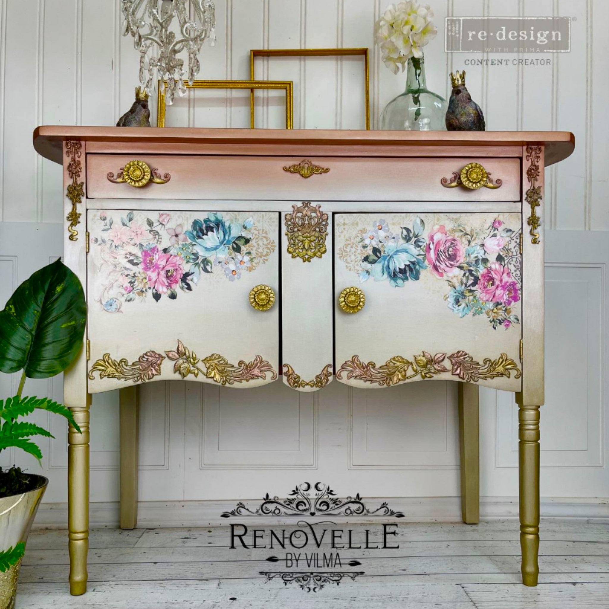 A vintage console table with storage refurbished by Renovelle by Vilma is painted an ombre blend of metallic salmon to white with gold legs and features ReDesign with Prima's Fuchsia Sunset rub on transfer on the 2 doors.