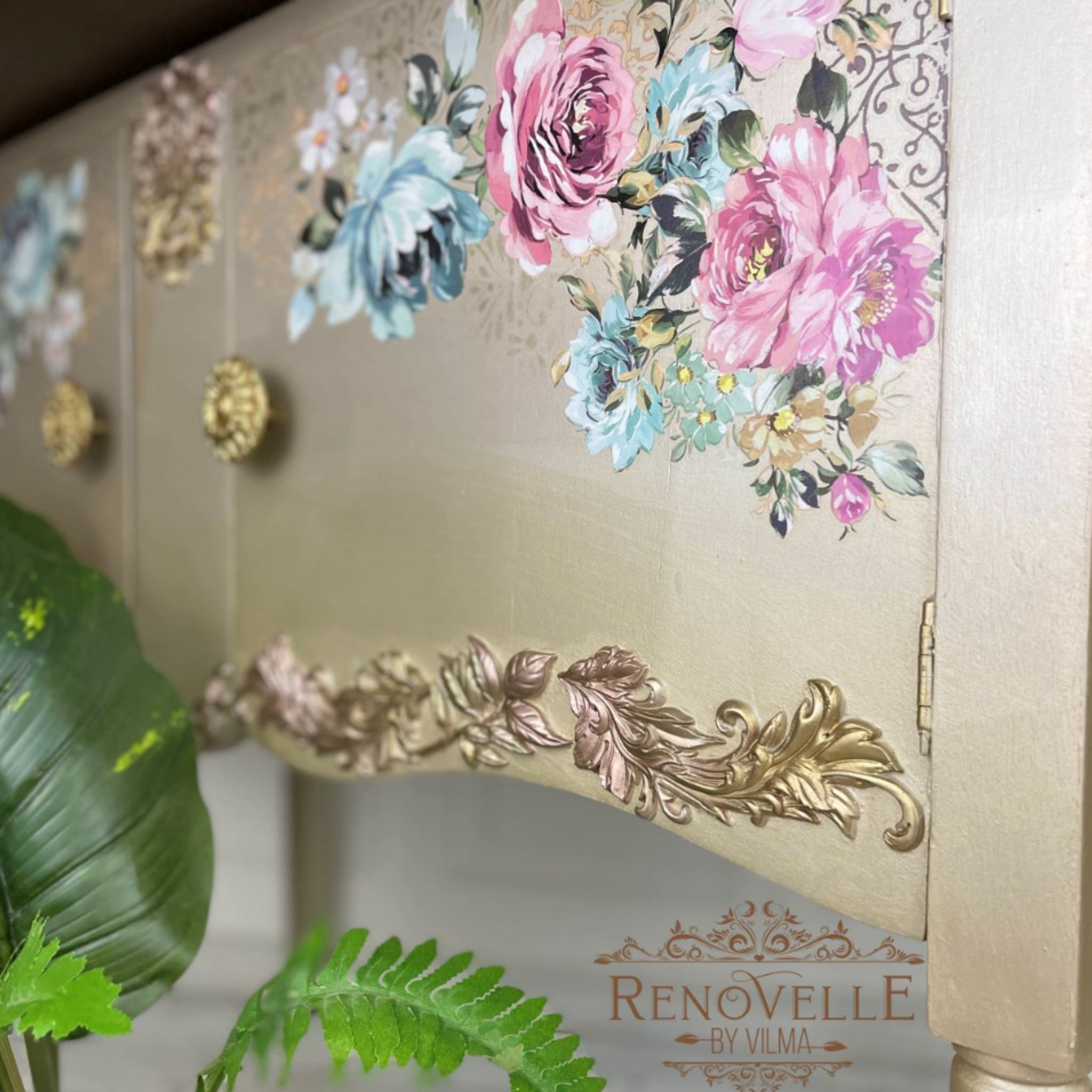 A close up of a vintage console table with storage refurbished by Renovelle by Vilma is painted an ombre blend of metallic salmon to white with gold legs and features ReDesign with Prima's Fuchsia Sunset rub on transfer on the 2 doors.