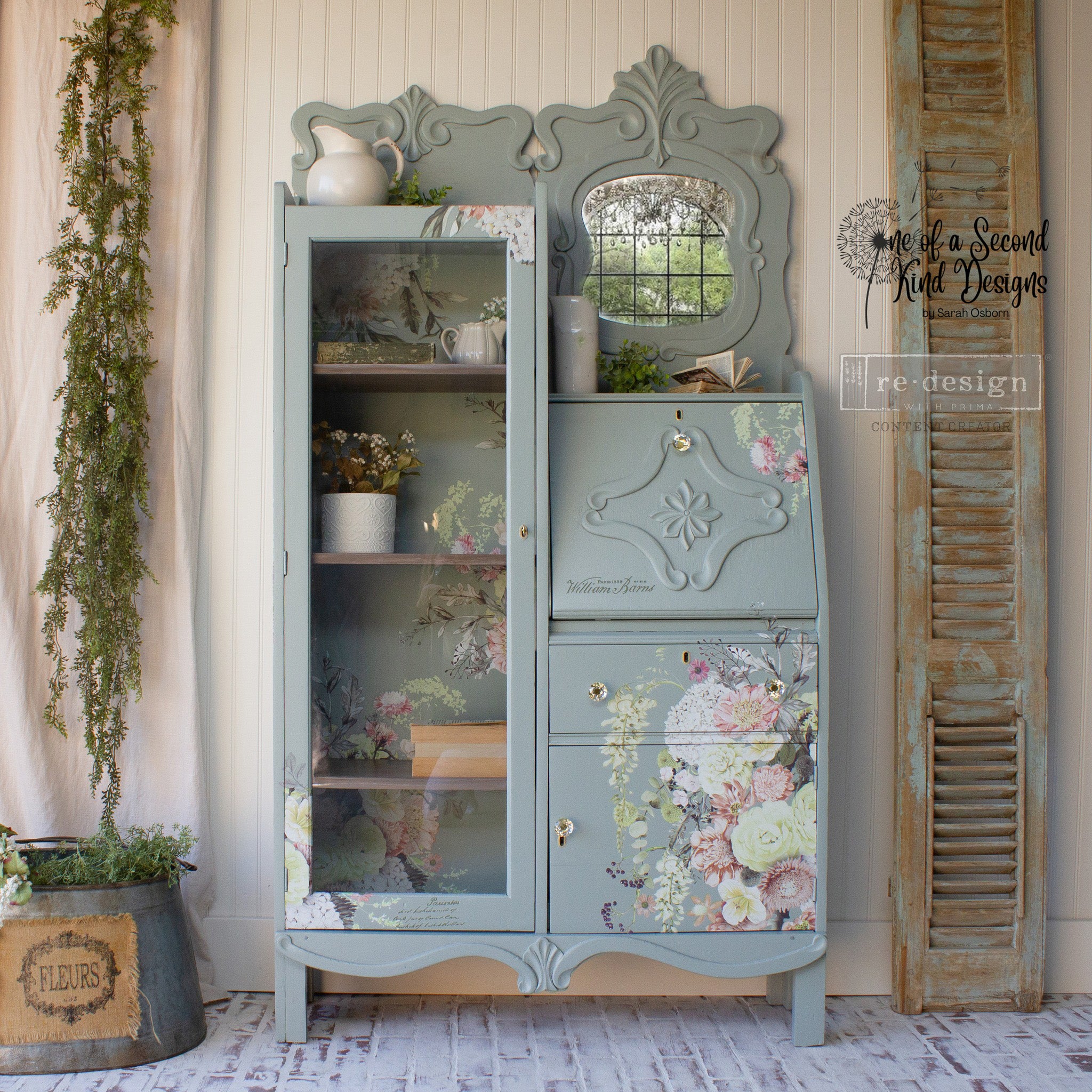 A vintage vanity cabinet refurbished by One of a Second Kind Designs is painted light gray and features ReDesign with Prima's Life in Full Bloom rub-on transfer on it.