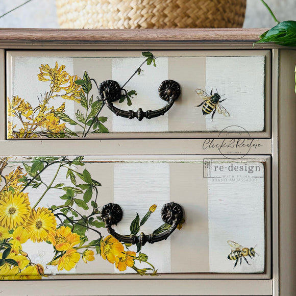 Close-up of a painted dresser showing Sunlit Serenade by ReDesign with Prima—yellow florals, green vines, and bee details applied across two drawers with dark vintage hardware