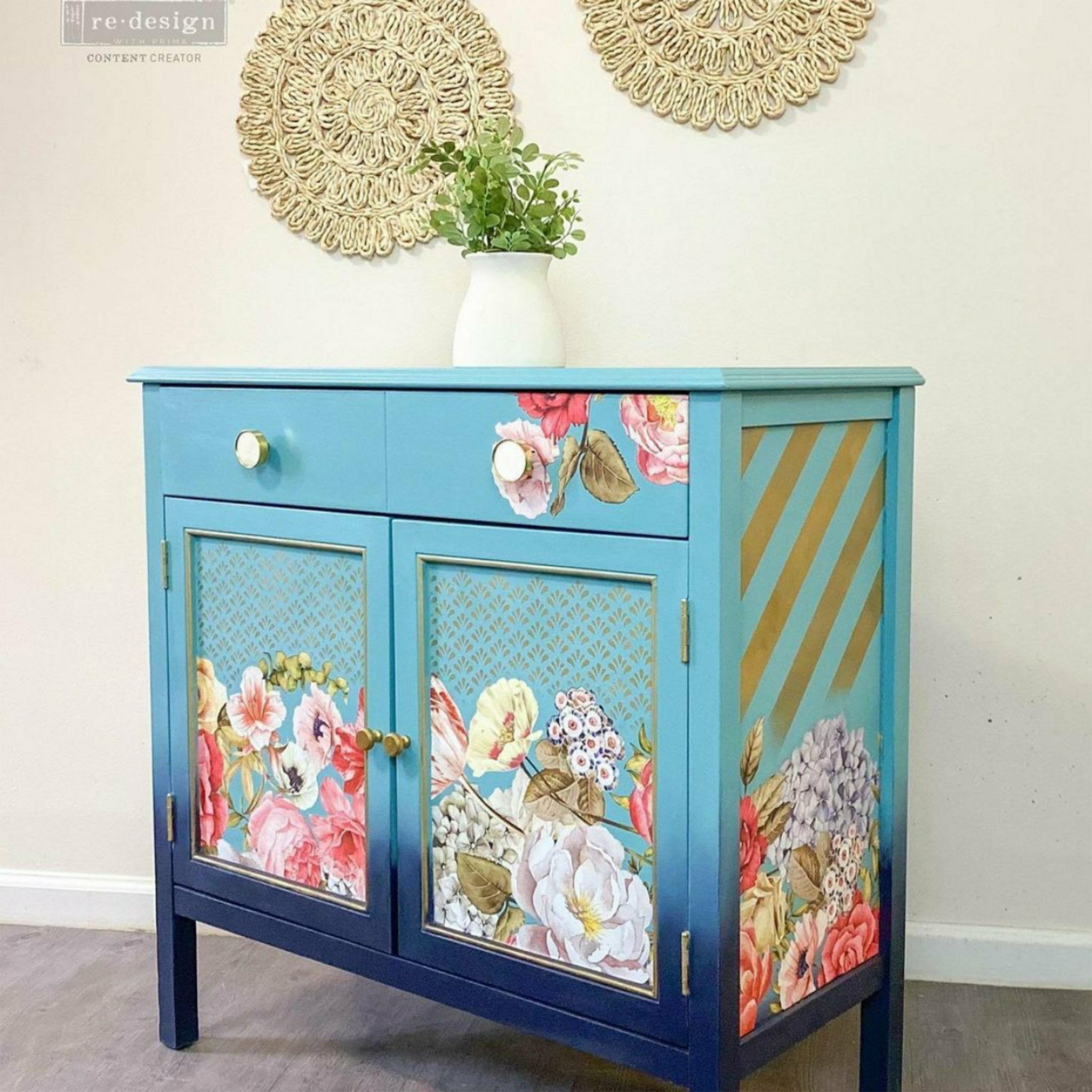 A vintage console table with storage is painted an ombre blend of light blue down to dark blue with gold accents and features ReDesign with Prima's Wondrous Floral 2 transfer on the front 2 doors, top right drawer, and on the side.