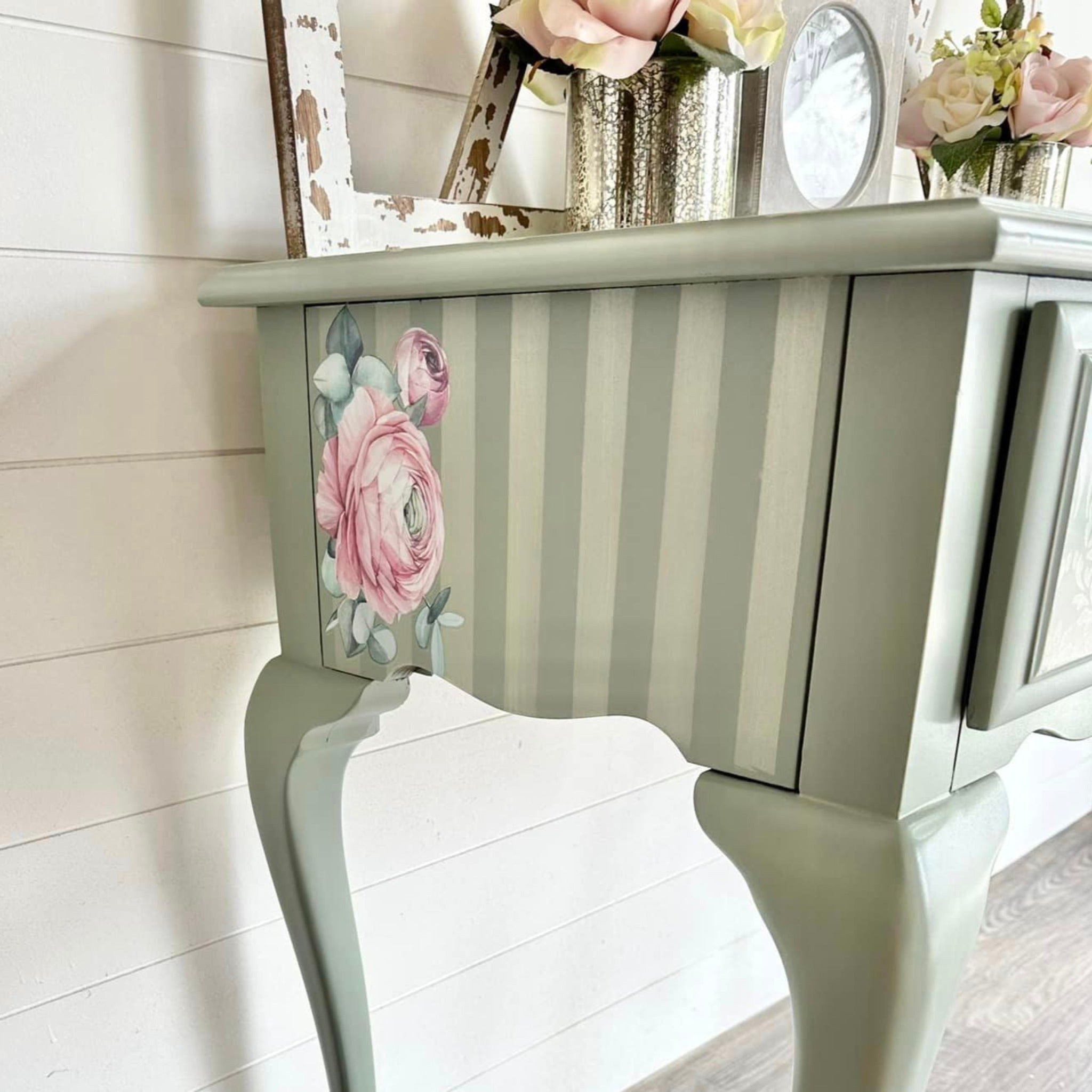 A side view of a vintage vanity desk that is painted light sage green has soft white stripes and features ReDesign with Prima's Overflowing Love transfer on the stripes.