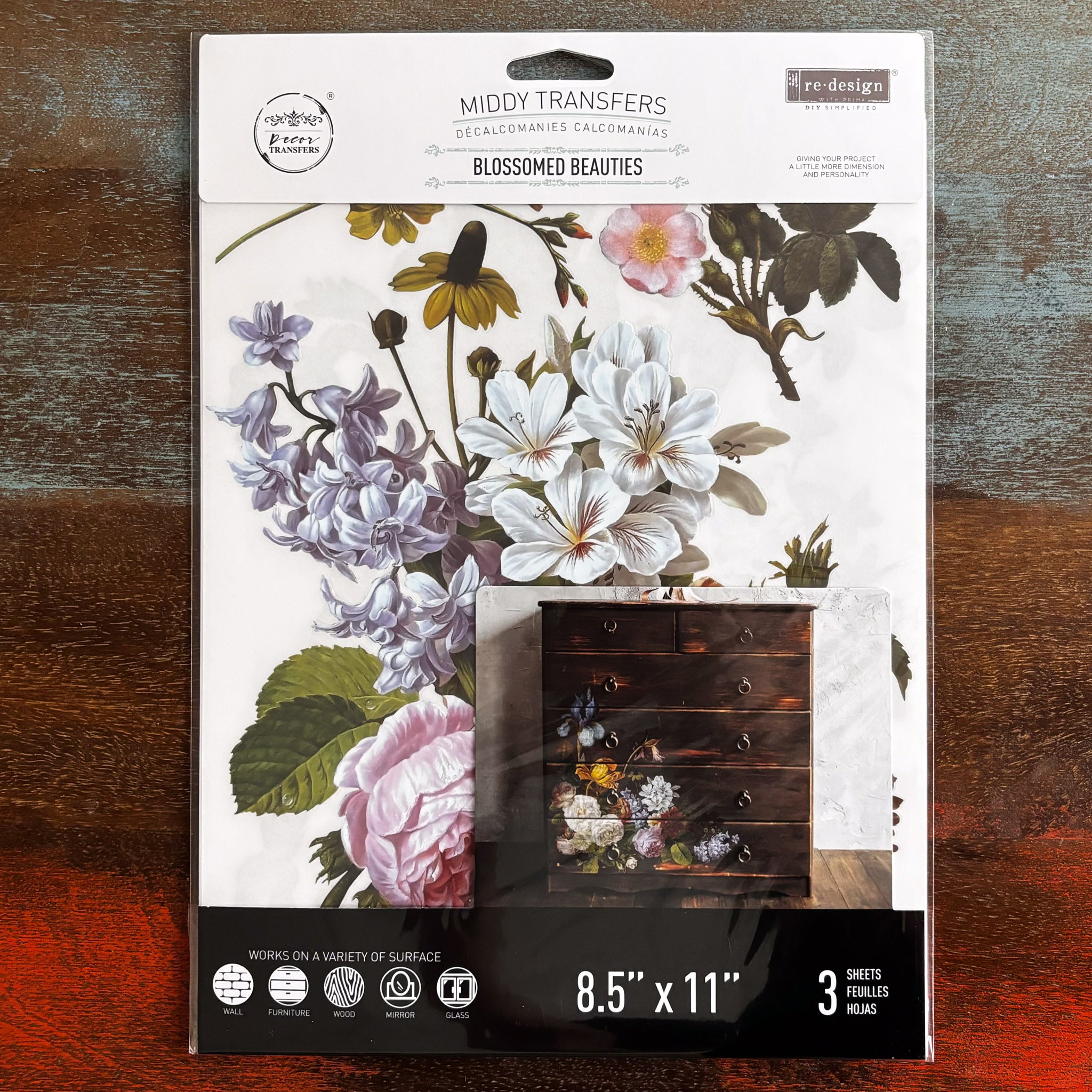 A package of ReDesign with Prima's Blossomed Beauties small transfer is against a dark wood background.