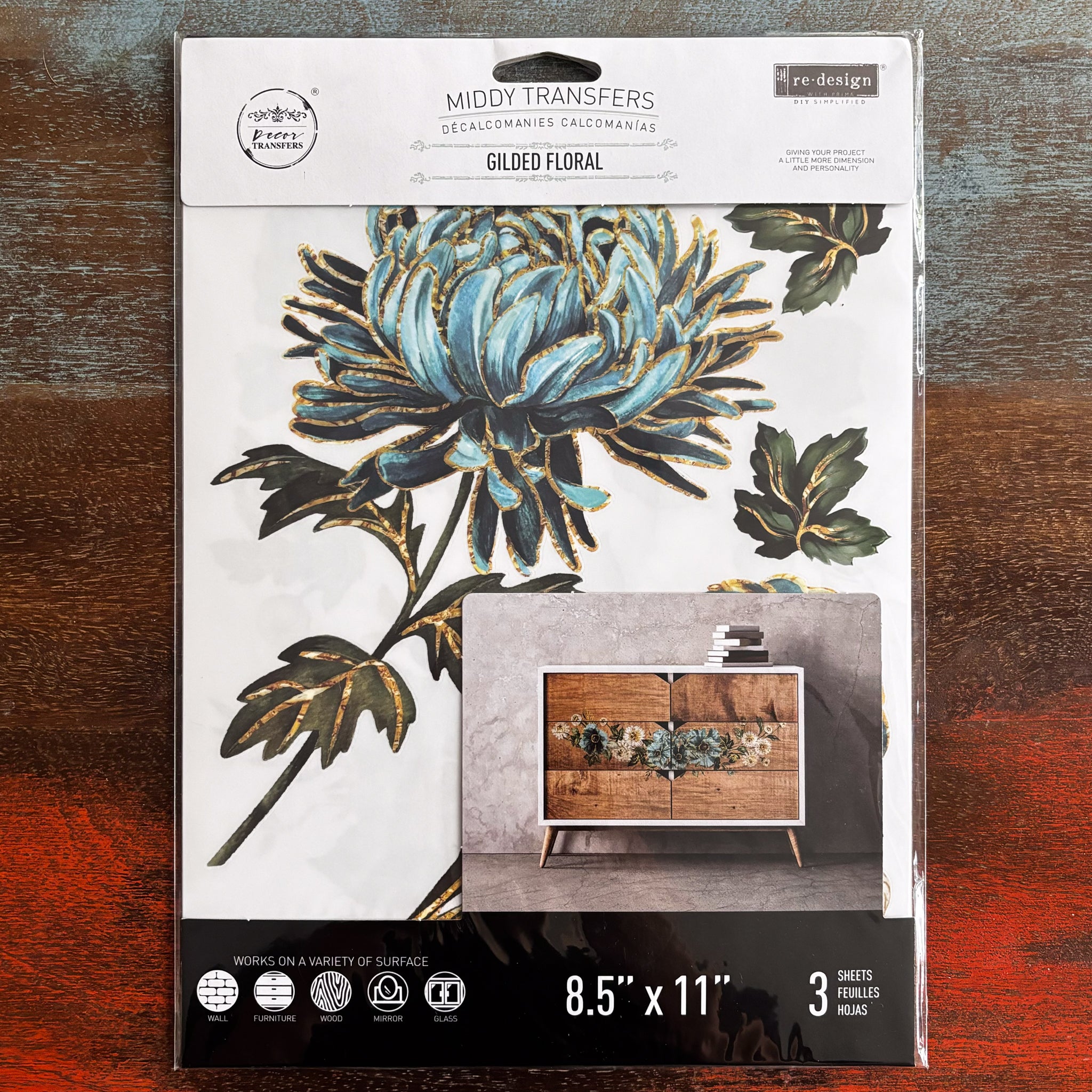 A package of ReDesign with Prima's Gilded Floral small transfer is against a dark wood background.