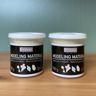 Two containers of re-design Modeling Material on a wooden surface with a gray background