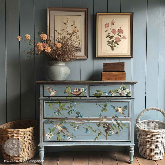 A 4-drawer dresser is painted a muted light blue and features ReDesign with Prima's Aviary Elegance rub-on furniture transfer on the front.