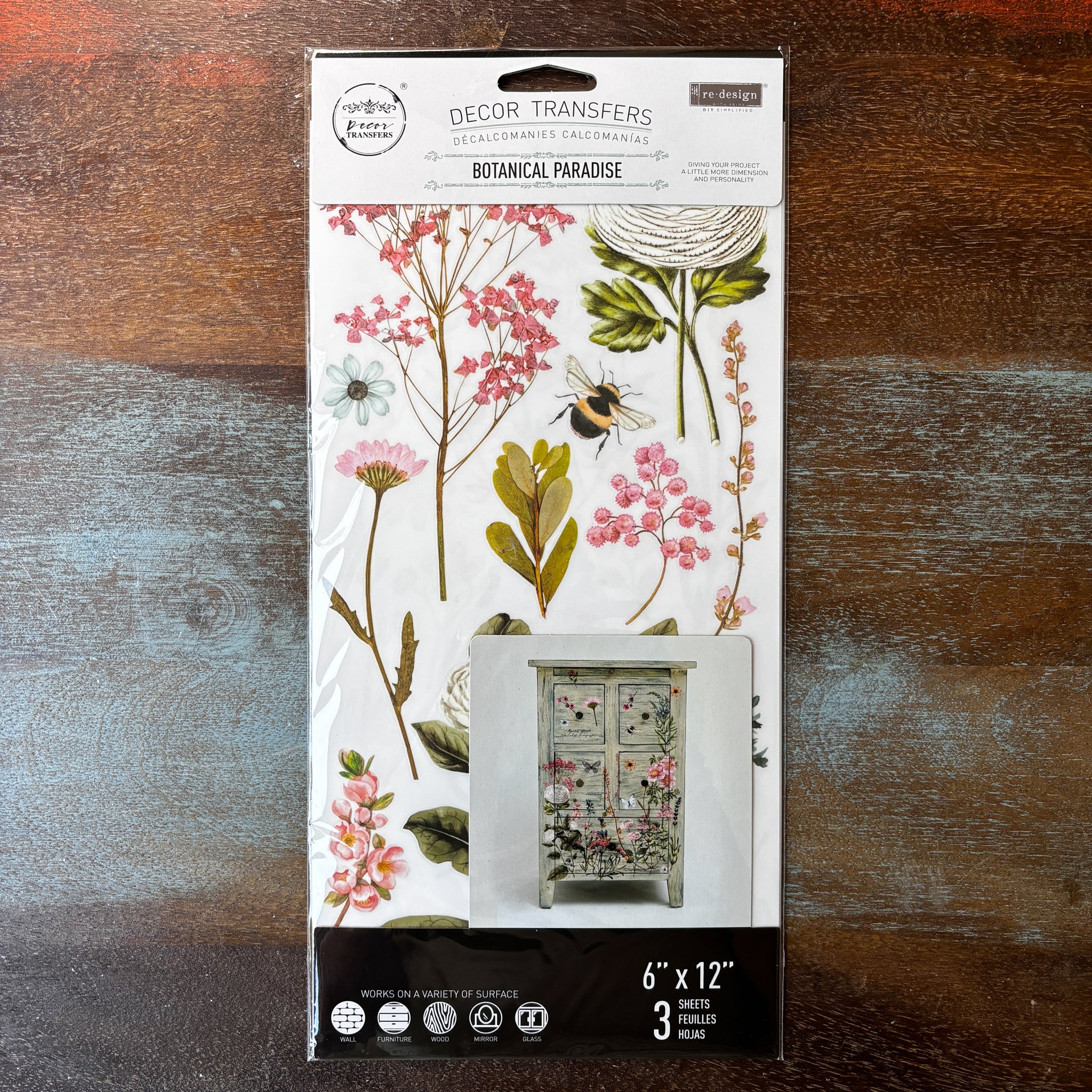 A package of ReDesign with Prima's Botanical Paradise small transfer is against a dark wood background.