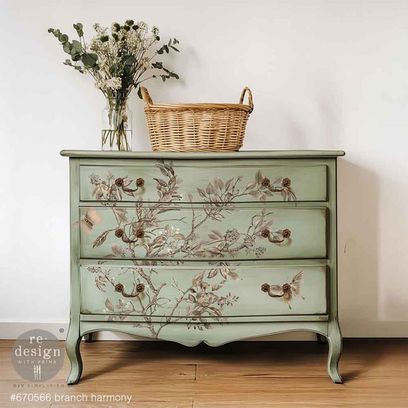 A 3-drawer dresser painted light sage green features ReDesign with Prima's Branch Harmony rub-on furniture transfer on the front.