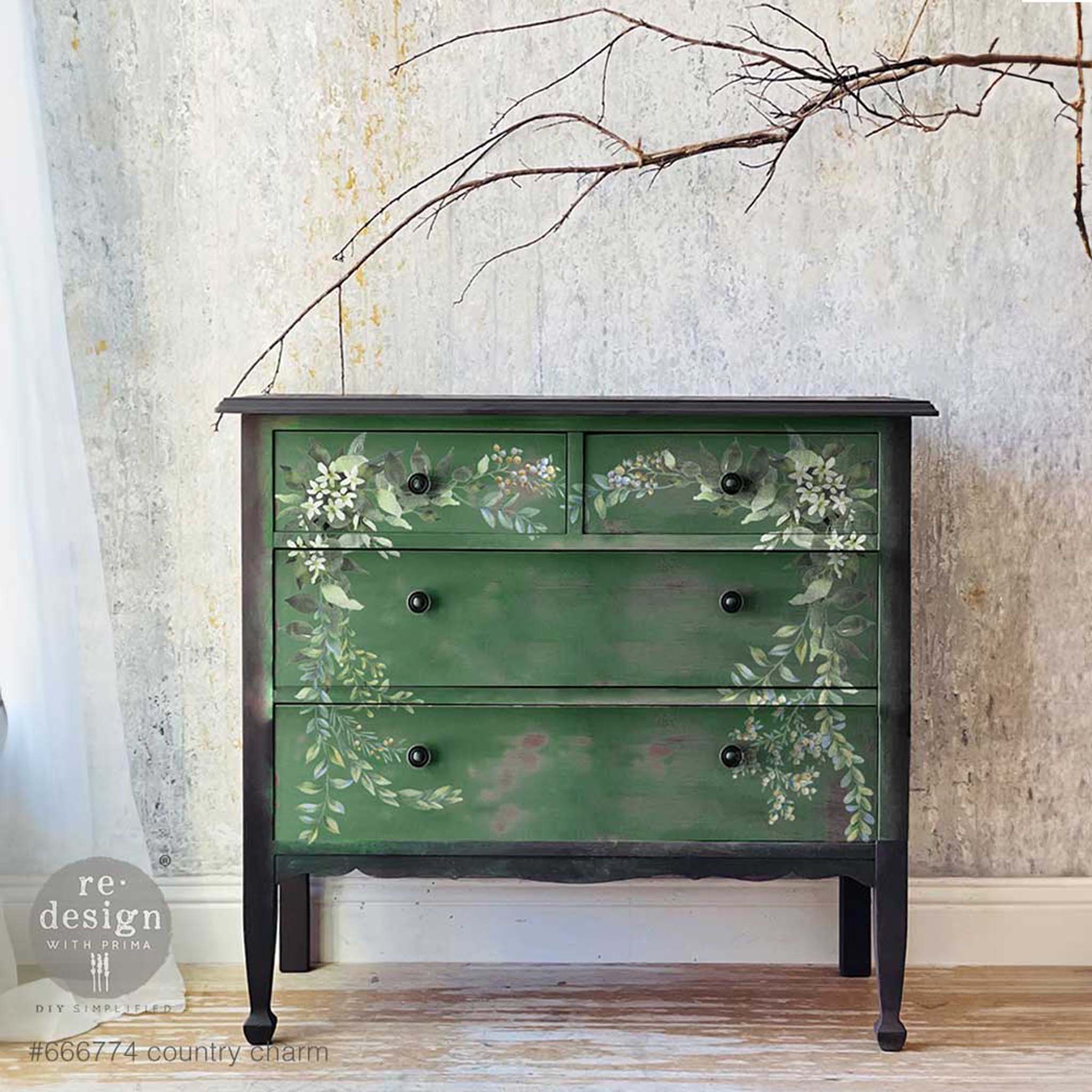 A vintage 4-drawer dresser is painted black with dark green on the drawers. ReDesign with Prima's Country Charm 12"x12" rub-on transfer is featured on the drawers.