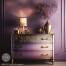 Decorative dresser with gold accents and a lamp against a purple wall.