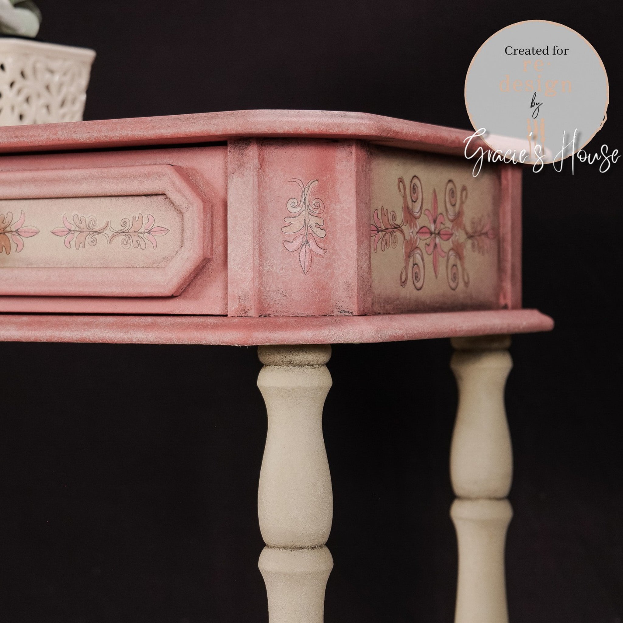 A vintage side table refurbished by Gracie's House is painted light pink and features ReDesign with Prima's Annie Sloan Flower Garland rub-on transfer on the front and side.