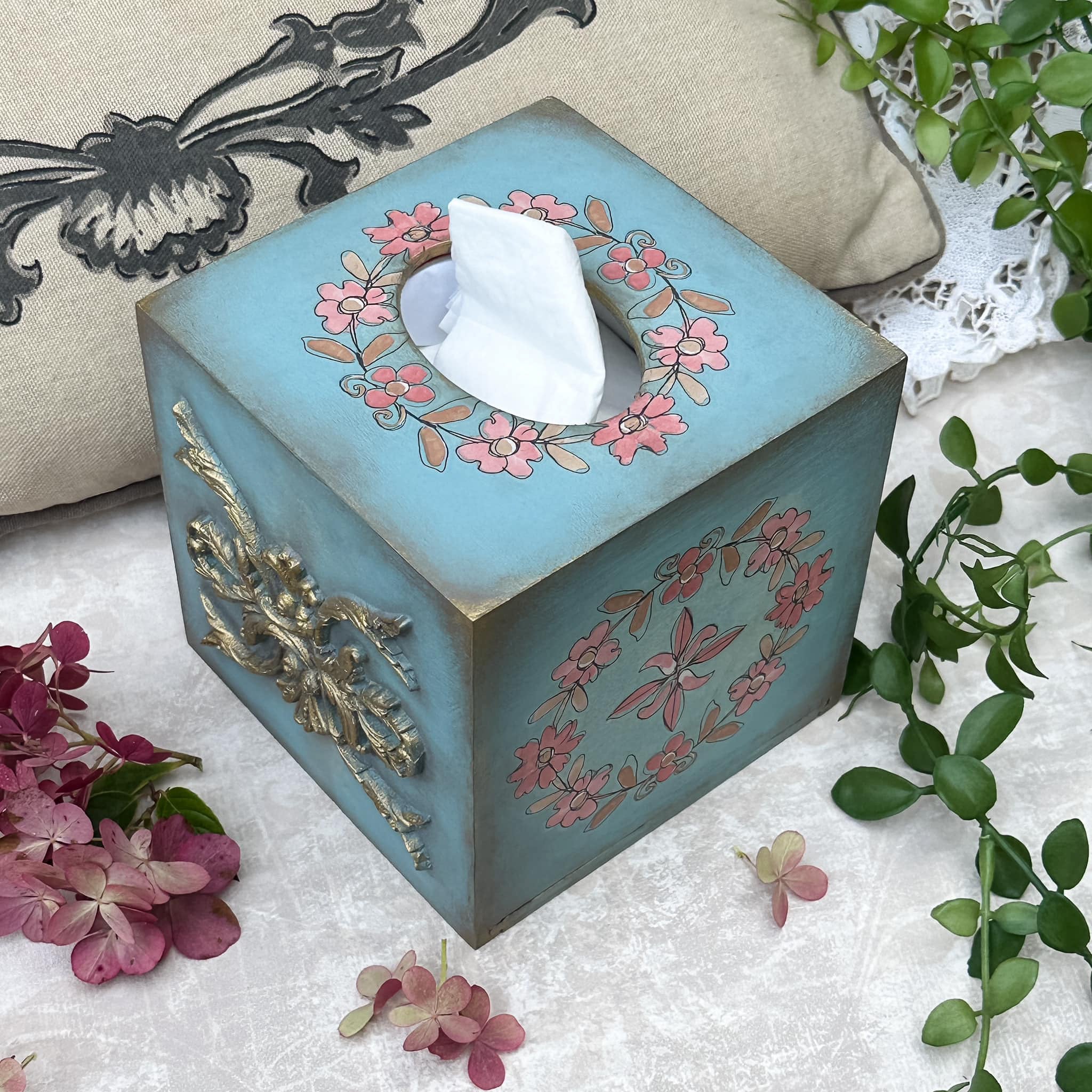 A wooden tissue box is painted pale blue and features ReDesign with Prima's Annie Sloan Flower Garland rub-on transfer on it.