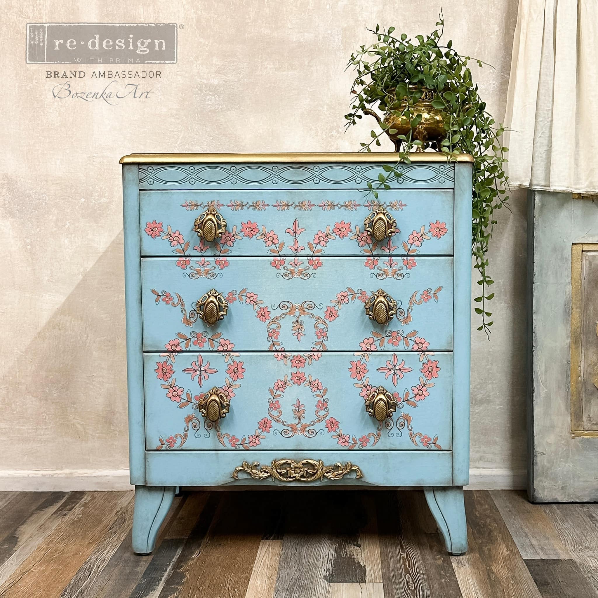 A vintage 3-drawer dresser refurbished by Bozenka Art is painted pale blue and features ReDesign with Prima's Annie Sloan Flower Garland rub-on transfer on its drawers.