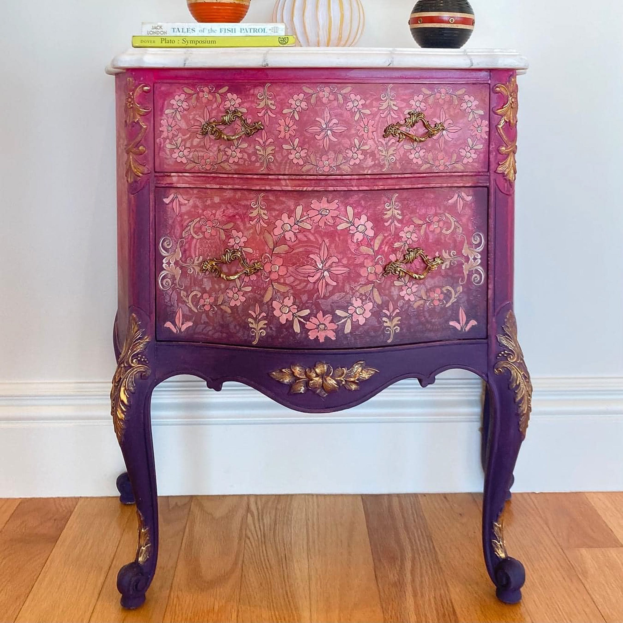 A vintage 2-drawer nightstand is painted an ombre of pink down to purple and features ReDesign with Prima's Annie Sloan Flower Garland rub-on transfer on its drawers.