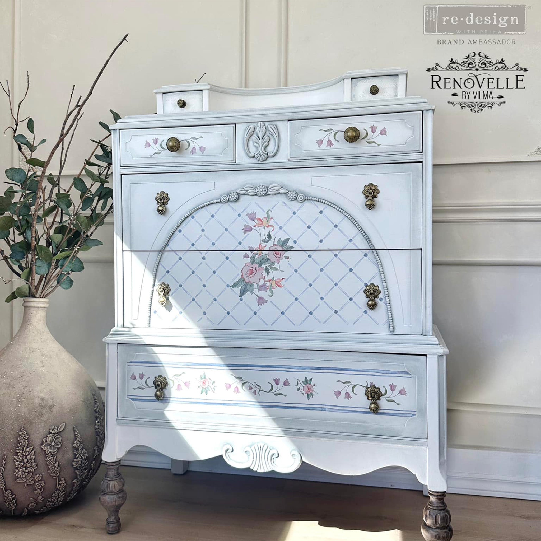 A vintage chest dresser refurbished by Renovelle by Vilma is painted white and light grey an features ReDesign with Prima's Annie Sloan Swedish Posy rub on transfer on the drawers.