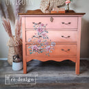 A vintage 3-drawer nightstand is painted an ombre of light to medium salmon pink and features ReDesign with Prima's Gentle Symphony rub-on transfer on the drawers.