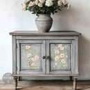 A vintage small buffet cabinet is painted grey with weathering and features ReDesign with Prima's Gentle Symphony small rub-on transfers on its 2 door inlays.