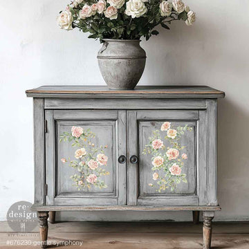 A vintage small buffet cabinet is painted grey with weathering and features ReDesign with Prima's Gentle Symphony small rub-on transfers on its 2 door inlays.