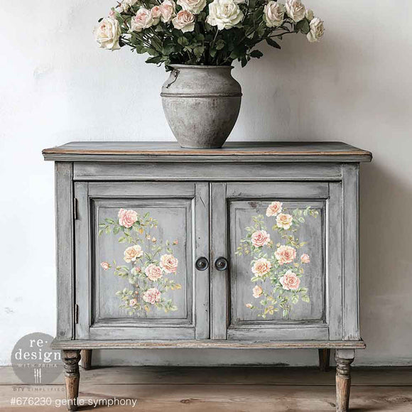 A vintage small buffet cabinet is painted grey with weathering and features ReDesign with Prima's Gentle Symphony small rub-on transfers on its 2 door inlays.