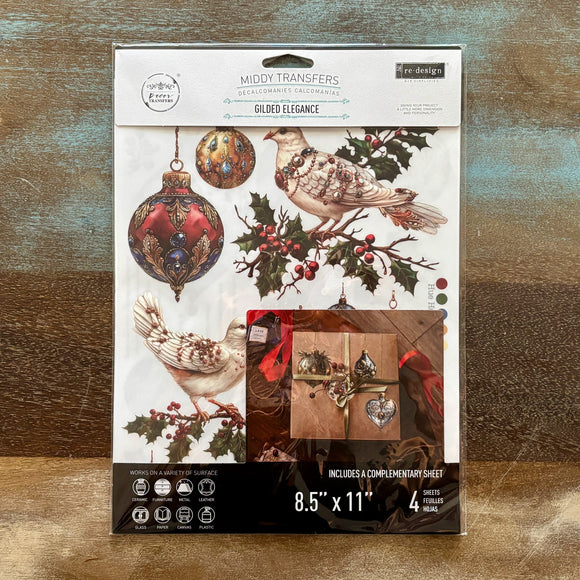 A package of ReDesign with Prima's Gilded Elegance middy rub-on transfers are against a wood background.