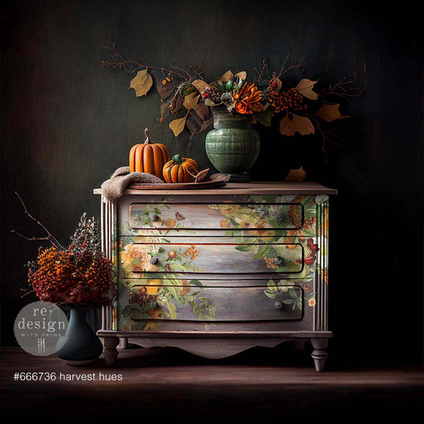 A vintage dresser is painted a blend of light grey and mauve and features ReDesign with Prima's Harvest Hues transfer on the front.